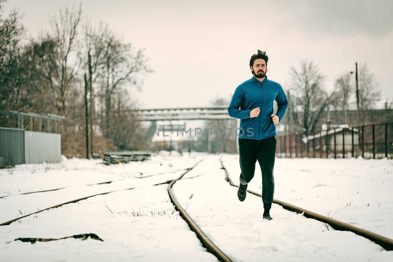 Active young man running and doing exercises across the old railroad during the winter training outside in. Copy space.