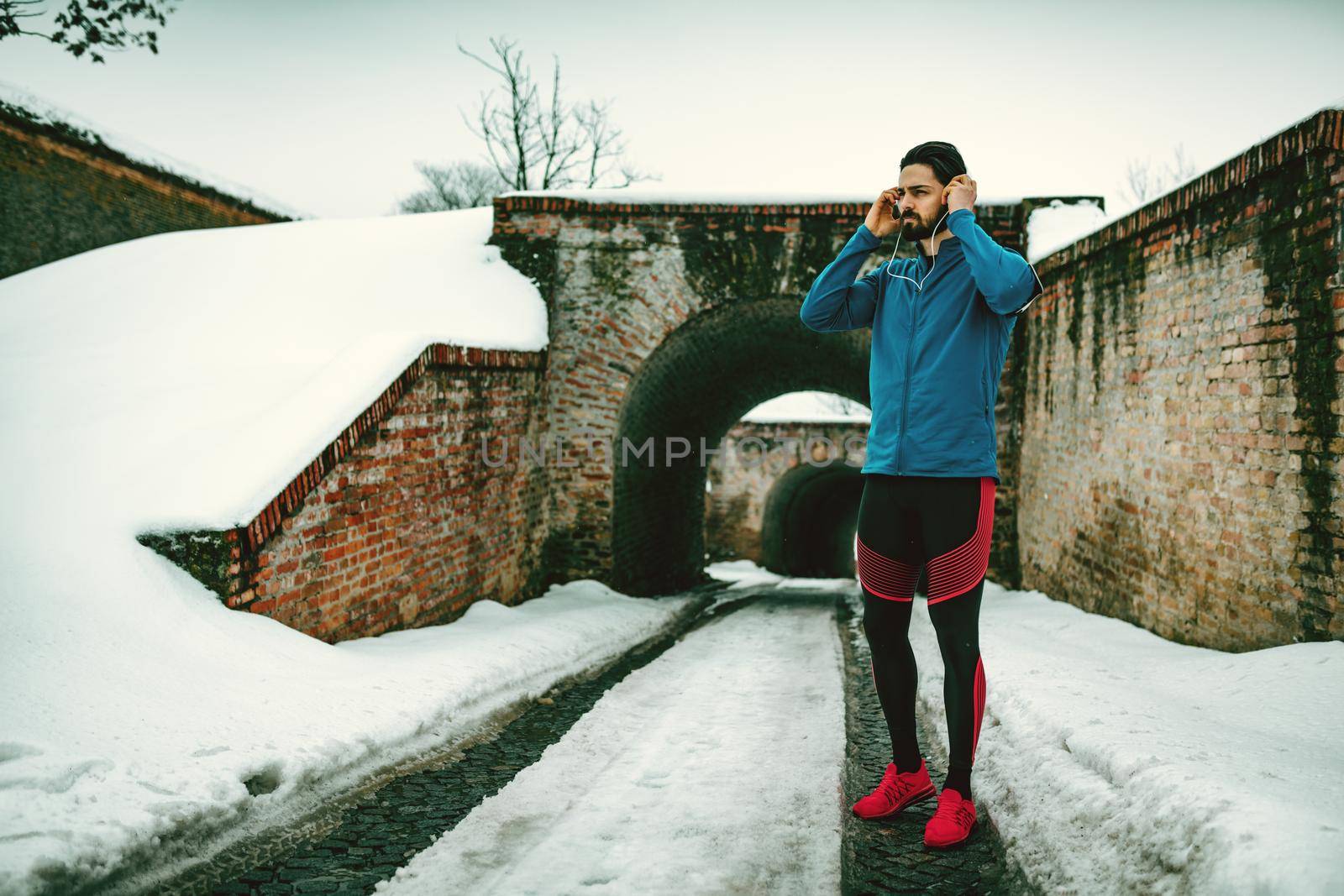 A male runner with headphones on his ears prepare to run in the public place during the winter training outside in. Copy space.