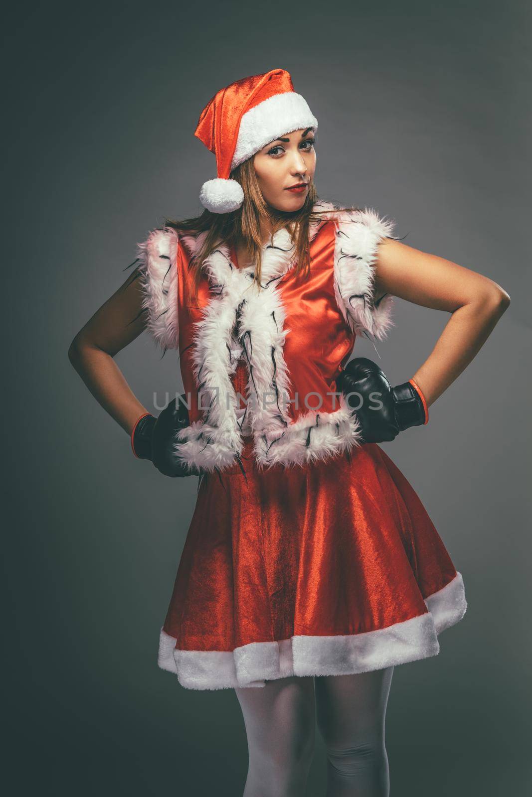 Beautiful young pensive woman in Santa Claus costume with boxing gloves.