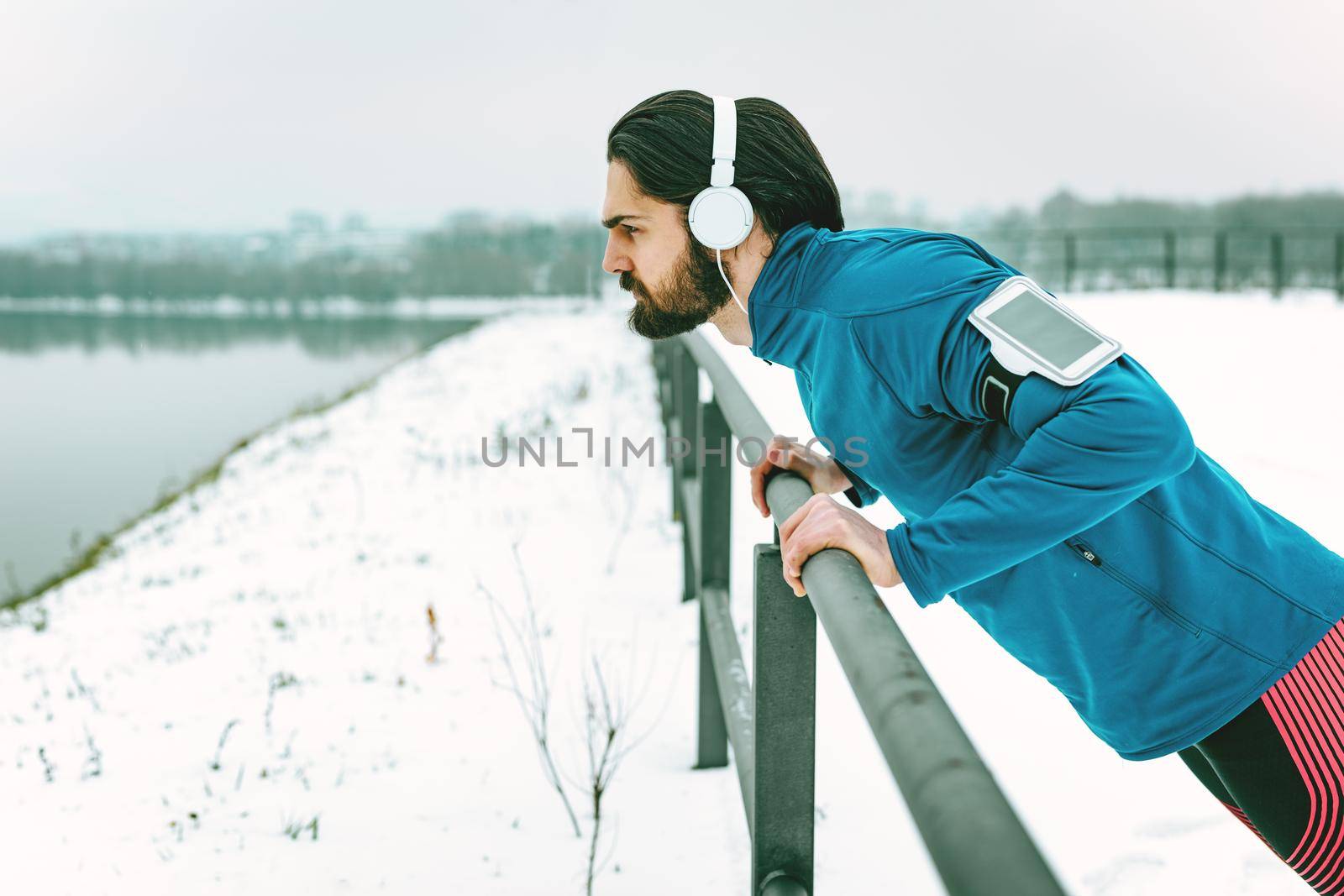 Young man athlete doing push ups and doing exercises during the winter training outside beside the river. Copy space.