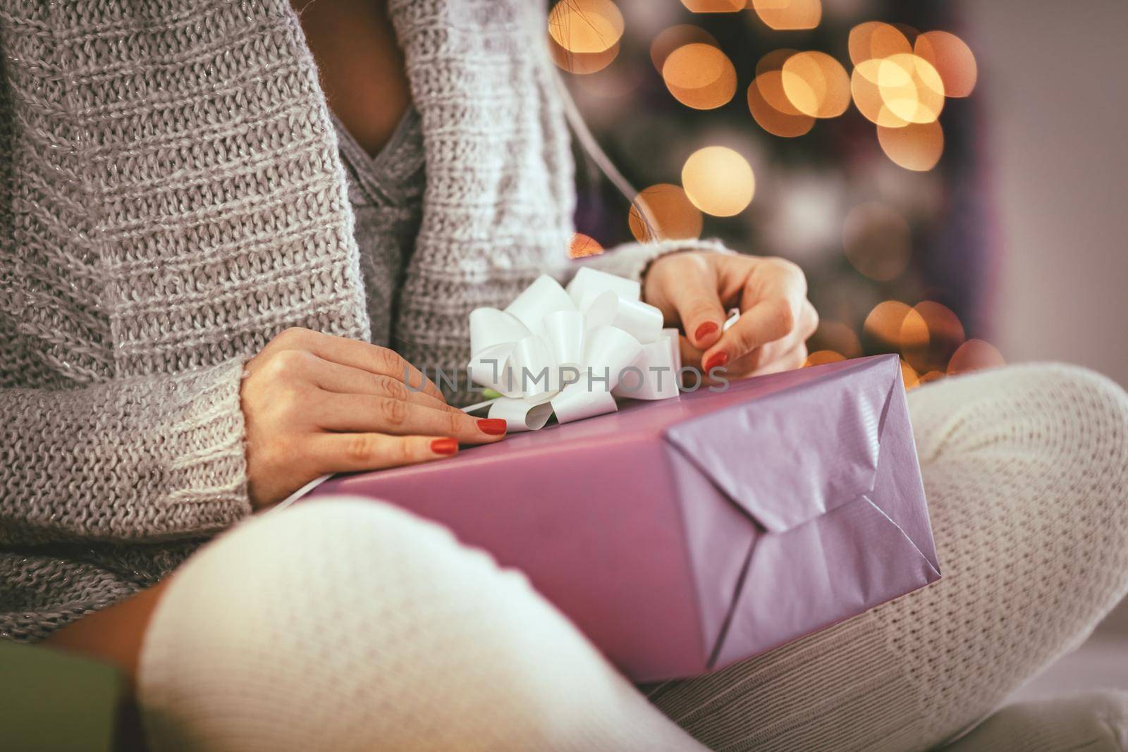 Close-up of a cute young woman holding gift and sitting in the bed with Christmas lights. 