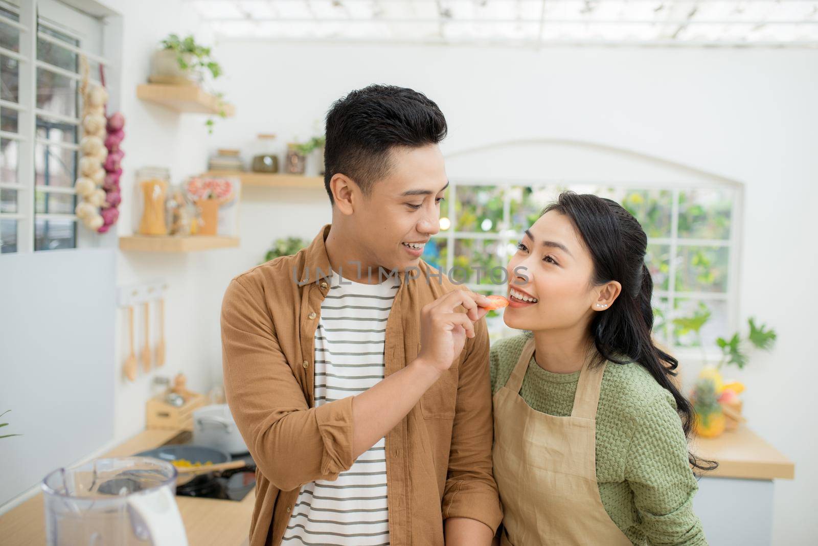 Beautiful happy asian couple are feeding each other in the kitchen. by makidotvn