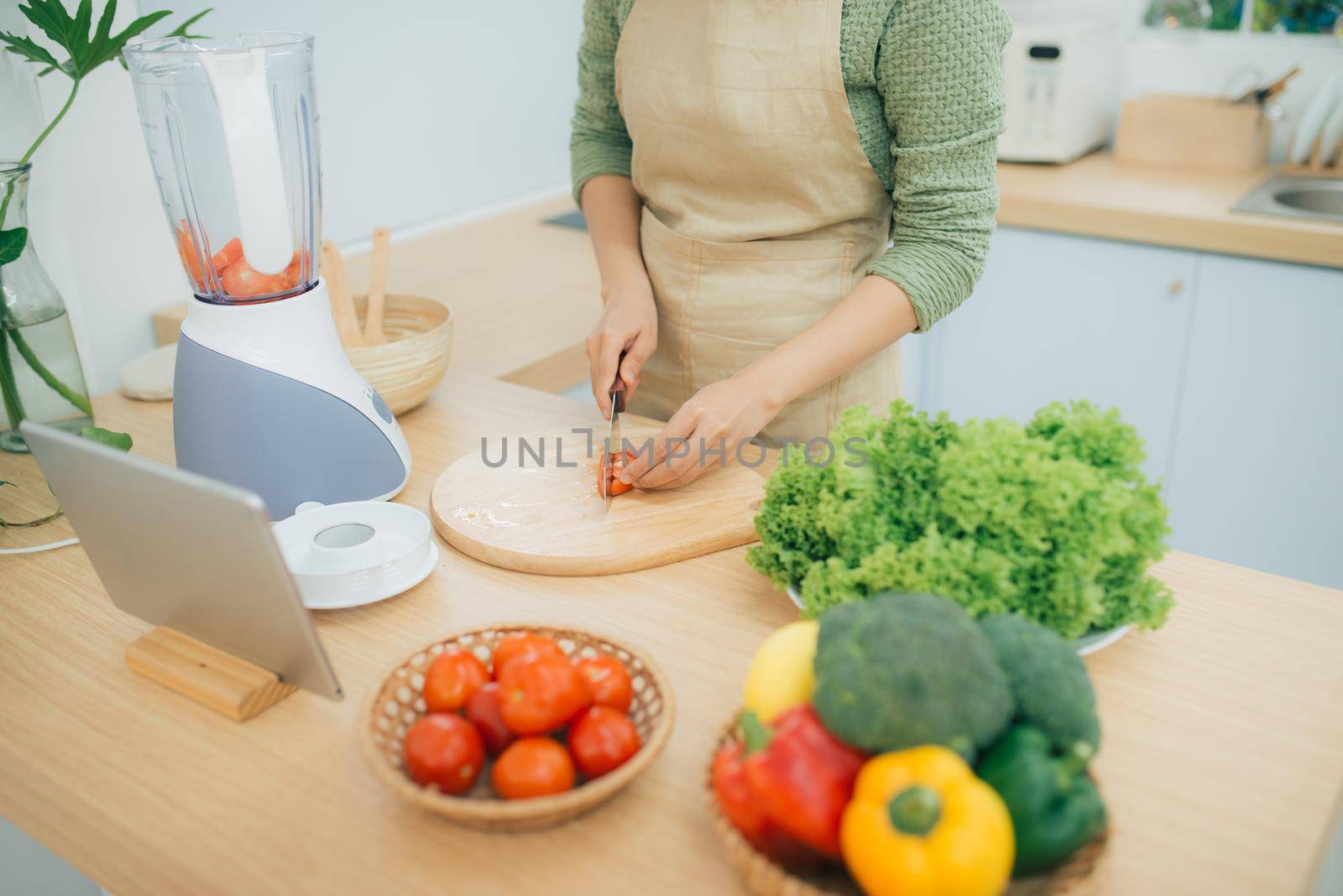 Image of young lady standing in kitchen using tablet computer and cooking vegetable salad