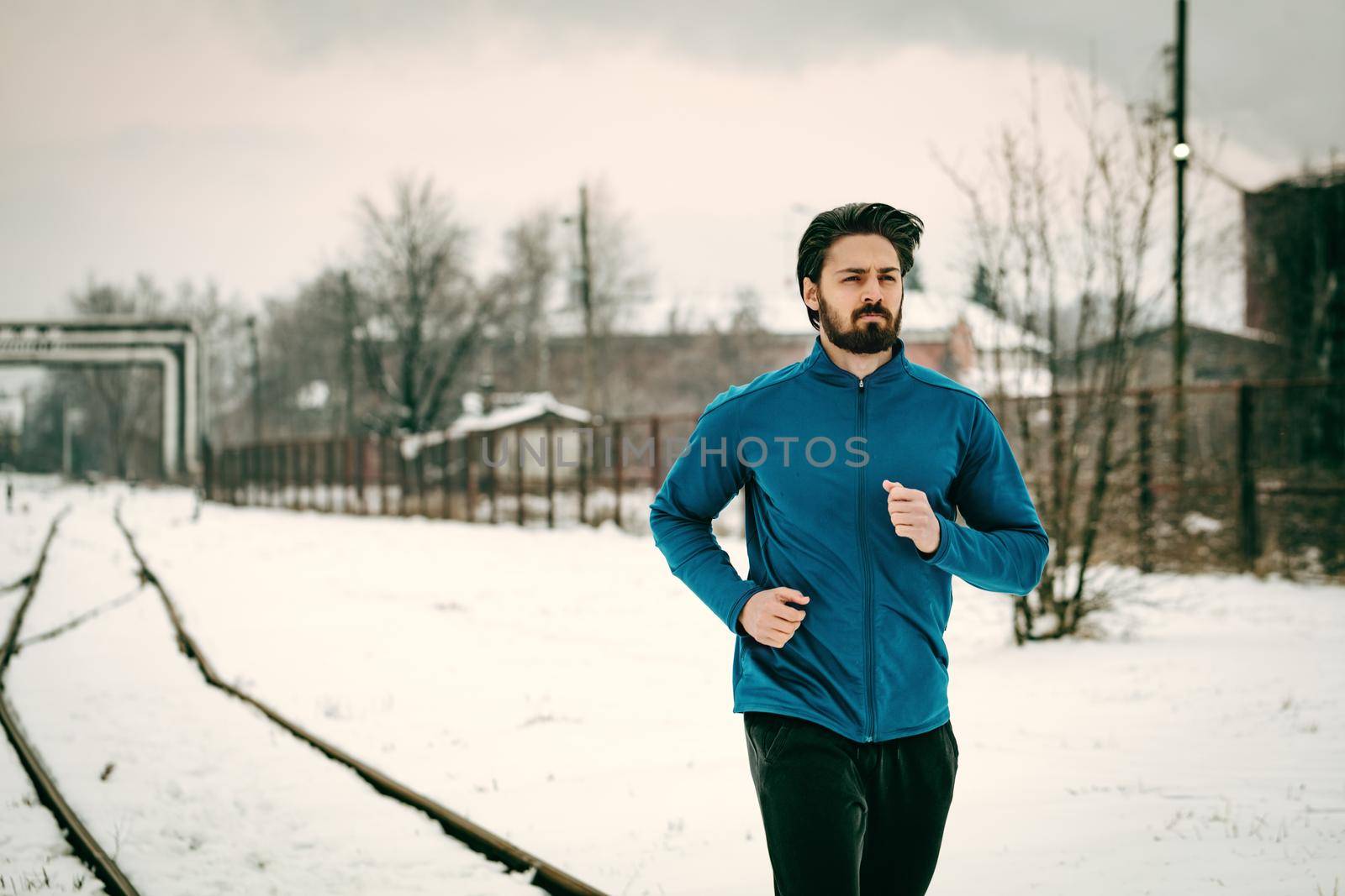 Active young man running and doing exercises across the old railroad during the winter training outside in. Copy space.