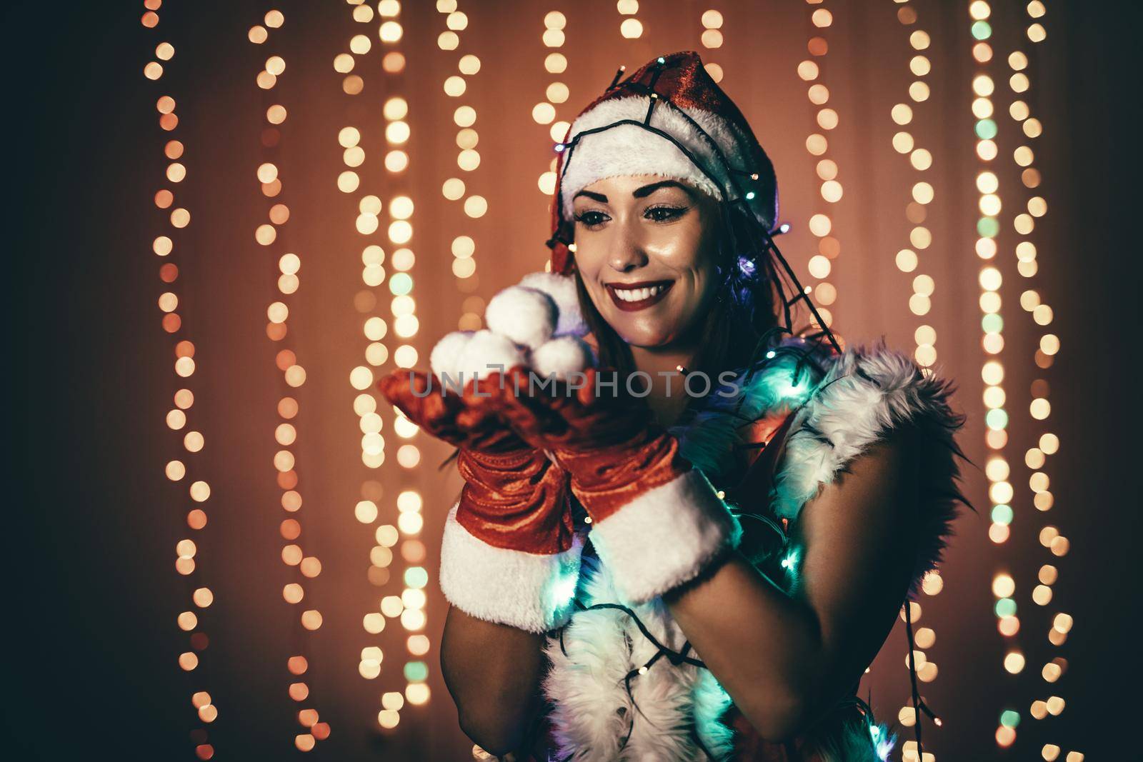 Portrait of a beautiful young smiling woman in Santa Claus costume holding snowballs.