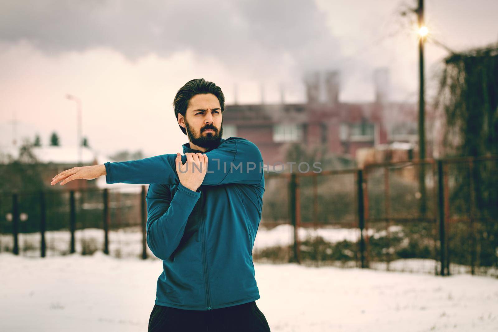 Active young man stretching and doing exercises in the old factory place among old railroad during the winter training outside in. Copy space. 