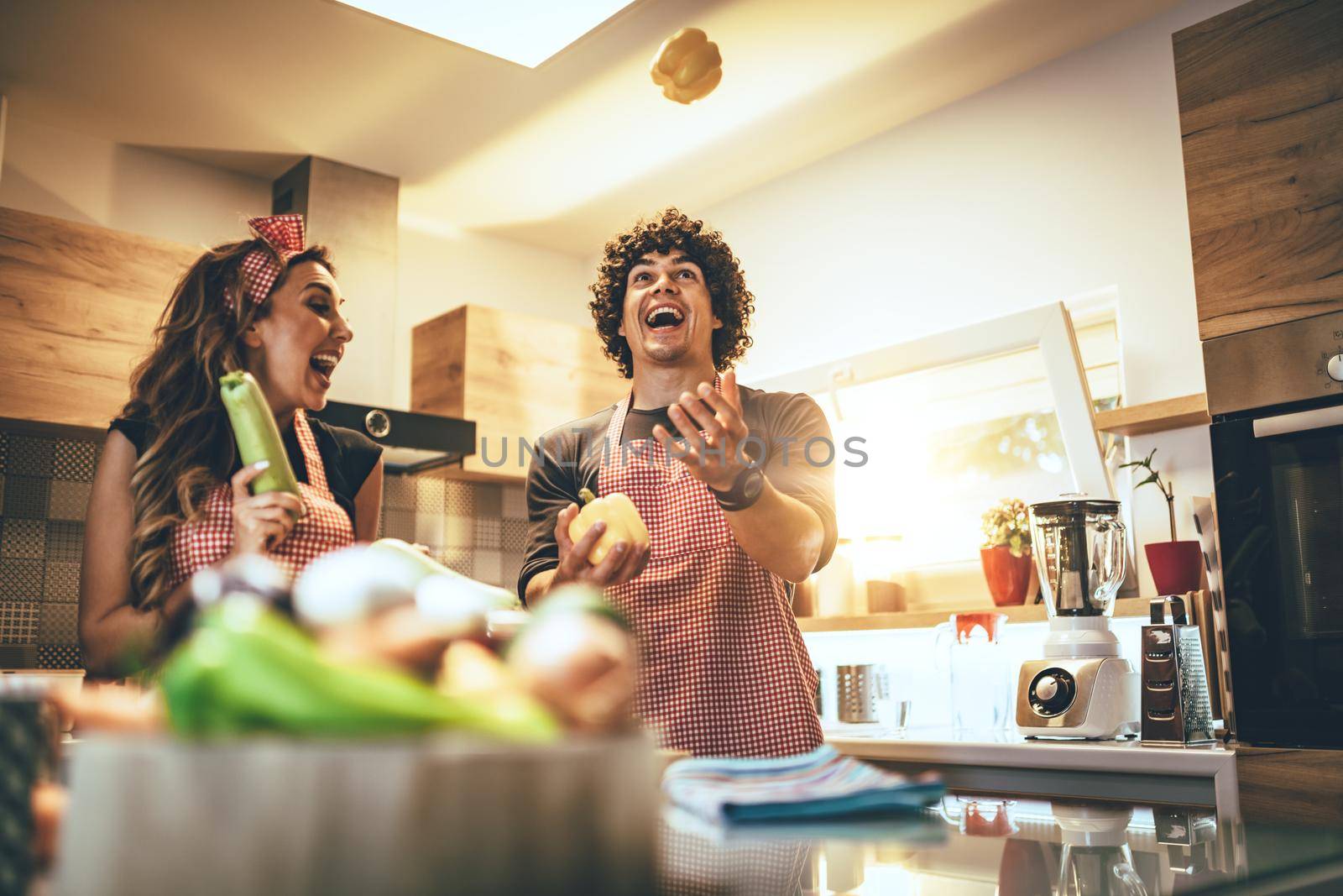 Happy young couple enjoys and having fun preparing vegetables and making healthy meal together at their home kitchen.  