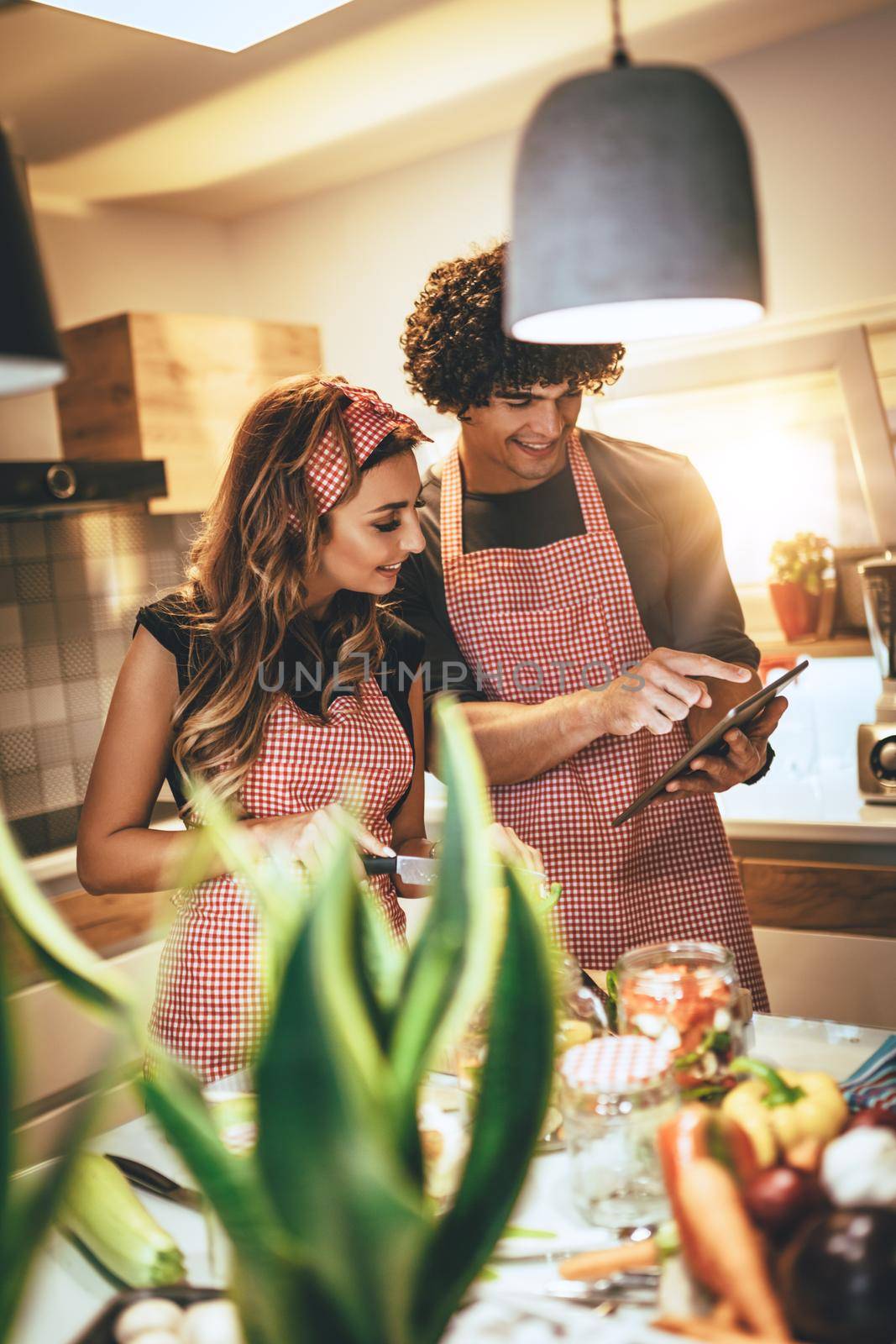 Young happy couple is enjoying and preparing healthy meal in their kitchen and reading recipes on the tablet.