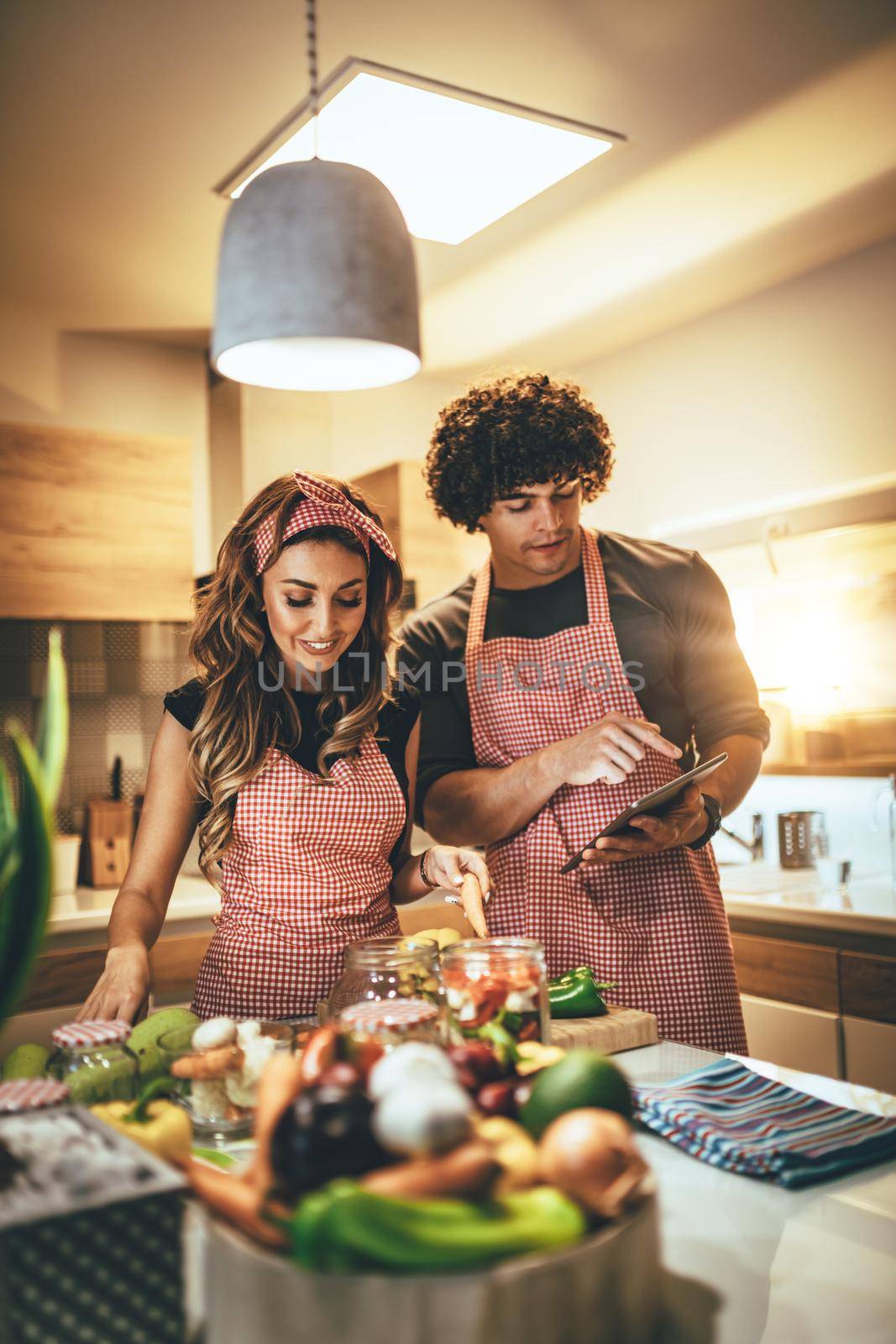 Young happy couple is enjoying and preparing healthy meal in their kitchen and reading recipes on the tablet.