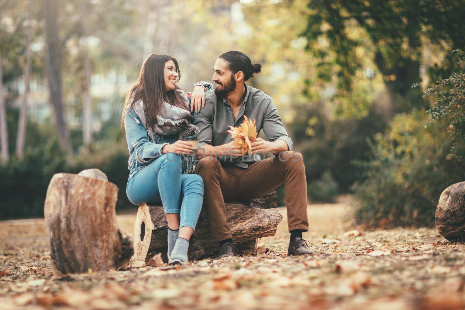 Beautiful smiling couple enjoying in sunny city park in autumn colors looking each other. They are embracing and holding yellow leaves.