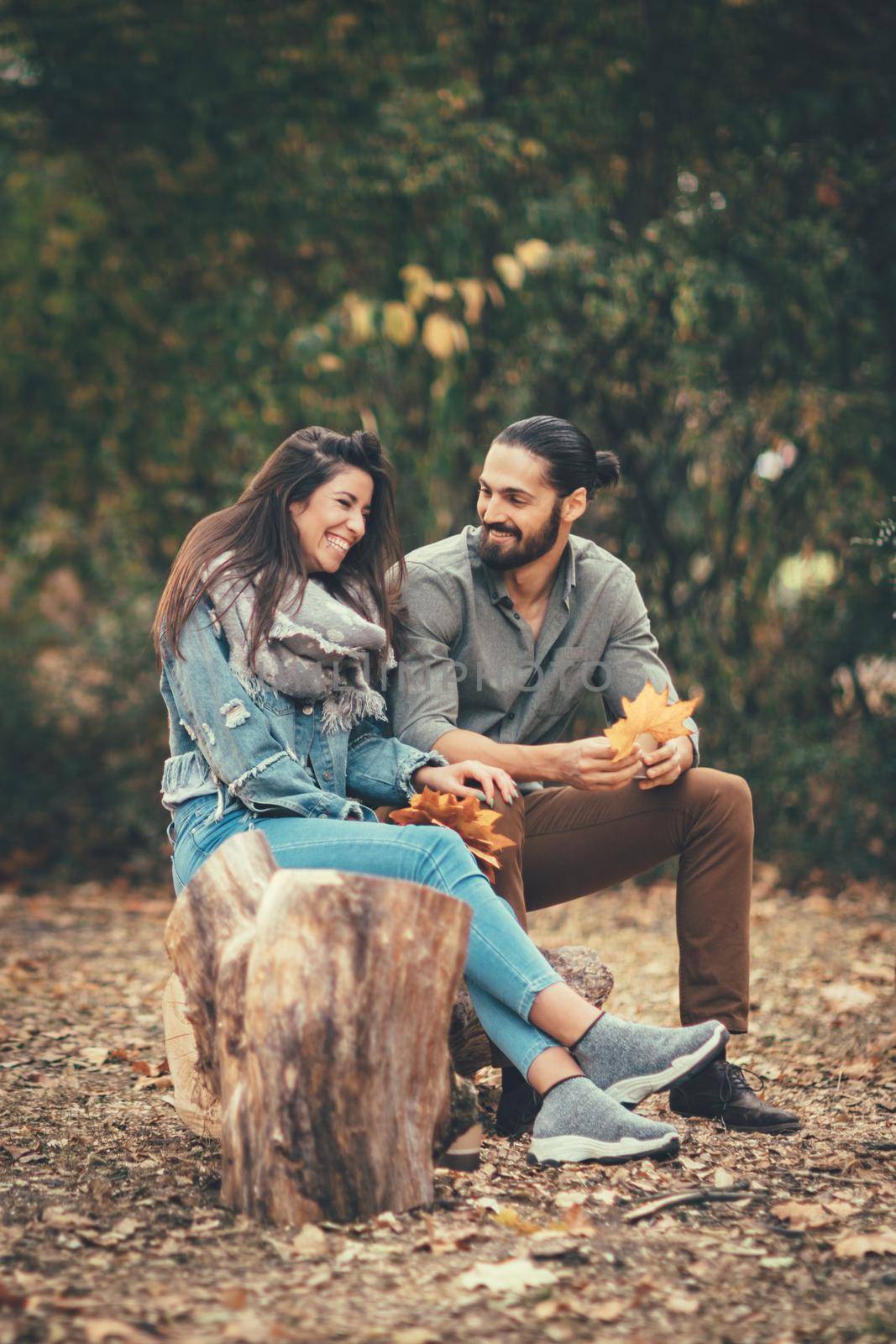 Beautiful smiling couple enjoying in sunny city park in autumn colors looking each other. They are having fun with yellow leaves.