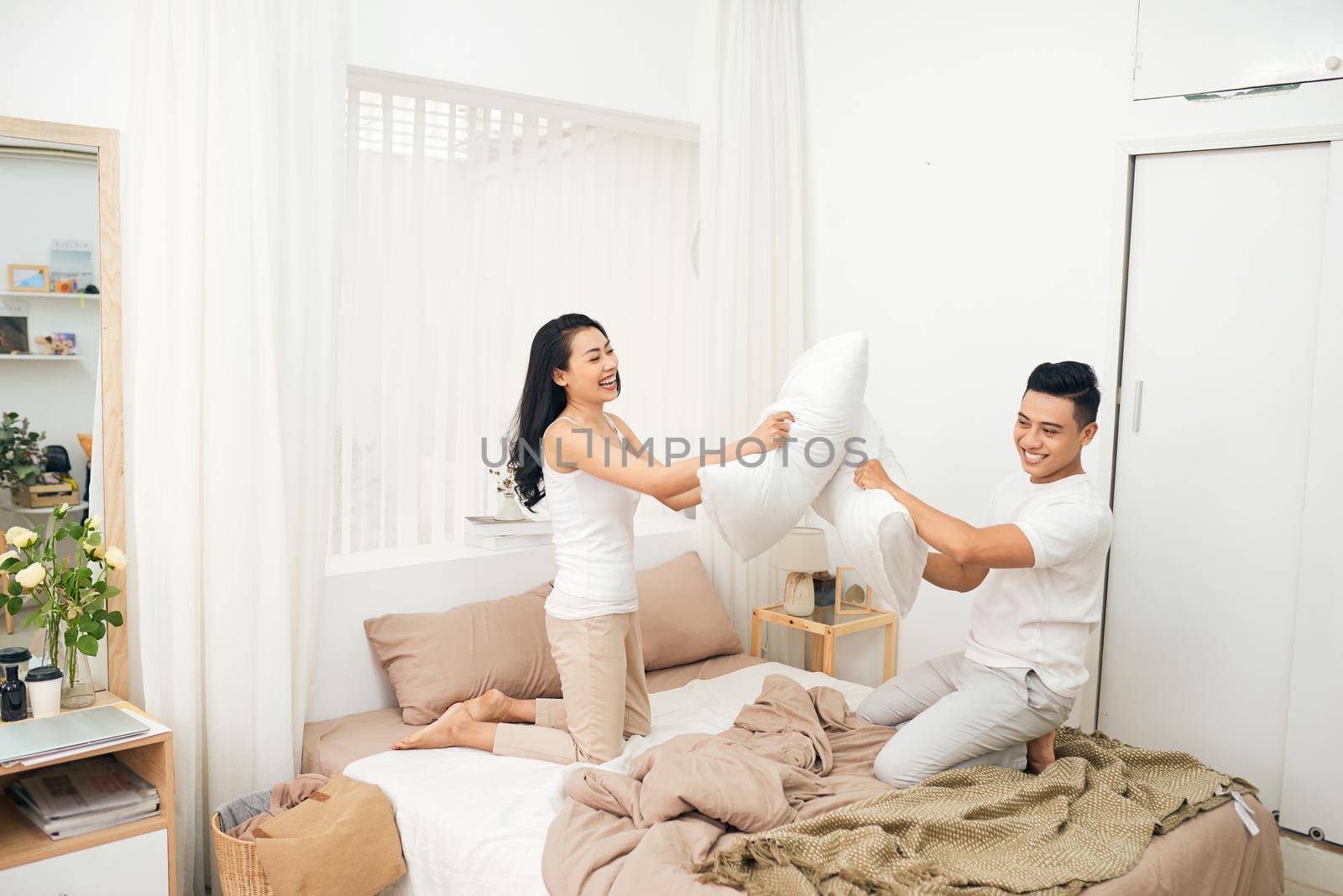 Young happy couple beat the pillows on the bed in a bedroom at home.