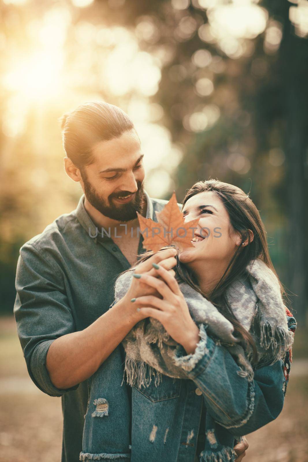 Portrait of a beautiful young couple in sunny forest in autumn colors. They are embracing and holding yellow leaf.