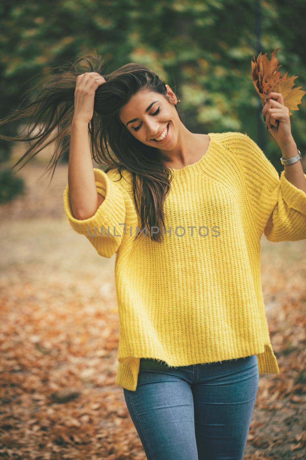 Cute young woman enjoying in sunny forest in autumn colors. She is holding golden yellow leaves  and having fun.