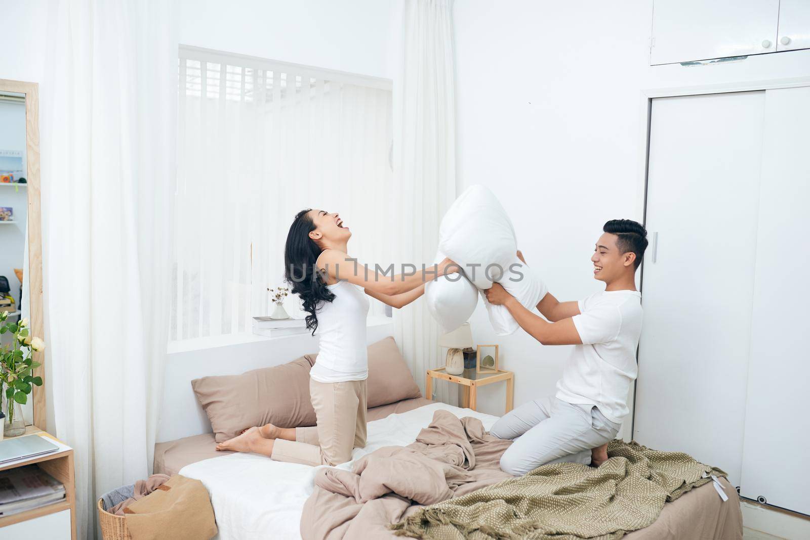 Young happy couple beat the pillows on the bed in a bedroom at home.