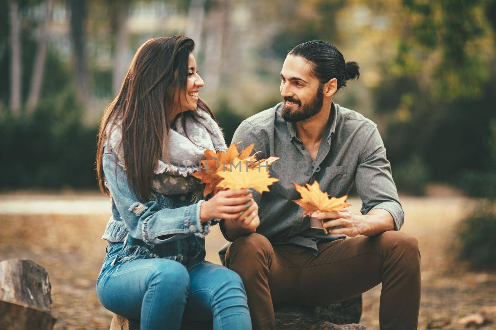 Beautiful smiling couple enjoying in sunny city park in autumn colors looking each other. They are having fun with yellow leaves.