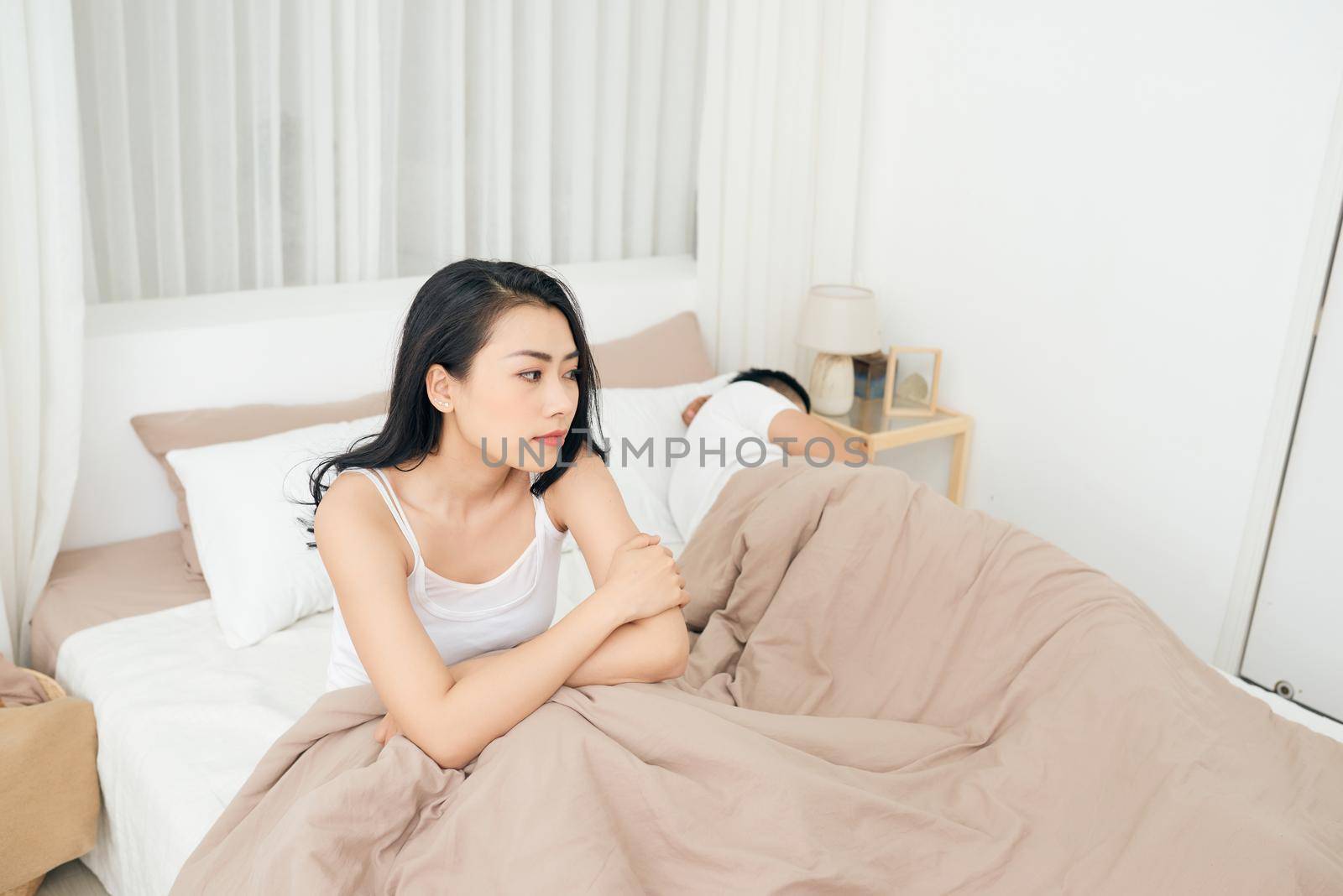 Unhappy Young Couple Sitting On Bed In Bedroom