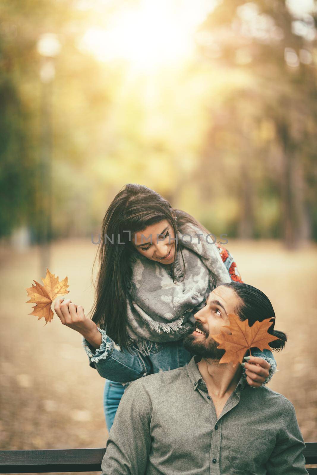 Beautiful smiling couple enjoying in sunny city park in autumn colors looking each other. They are having fun with yellow leaves.