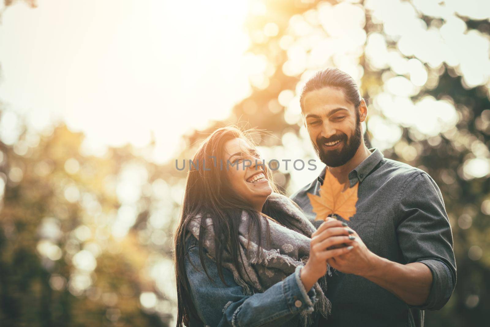 Portrait of a beautiful young couple in sunny forest in autumn colors. They are embracing and holding yellow leaf.