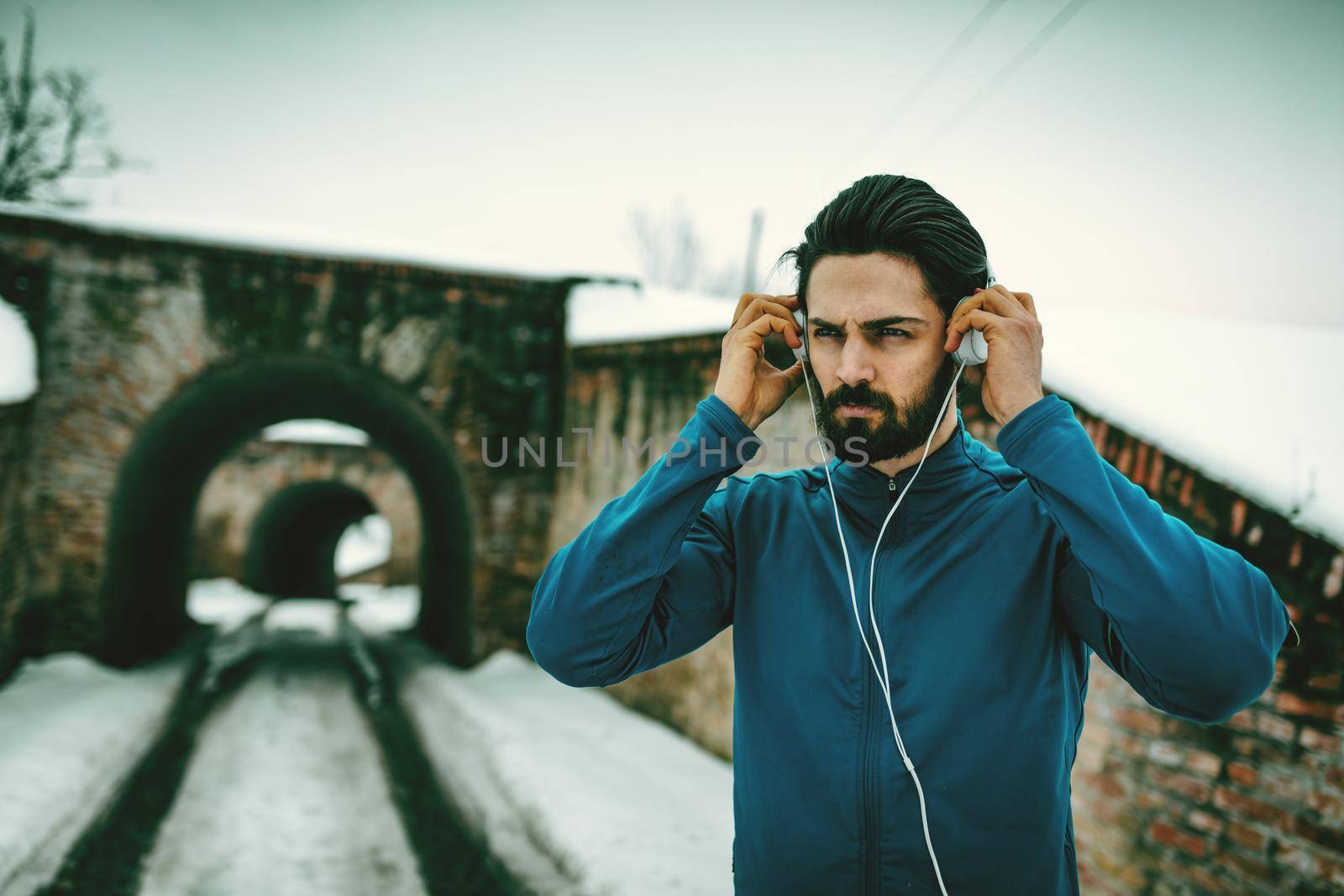 A male runner with headphones on his ears prepare to run in the public place during the winter training outside in. Copy space.