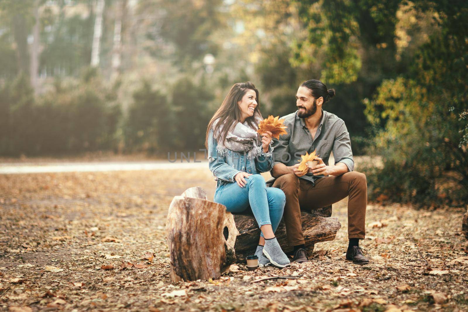 Beautiful smiling couple enjoying in sunny city park in autumn colors looking each other. They are having fun with yellow leaves.