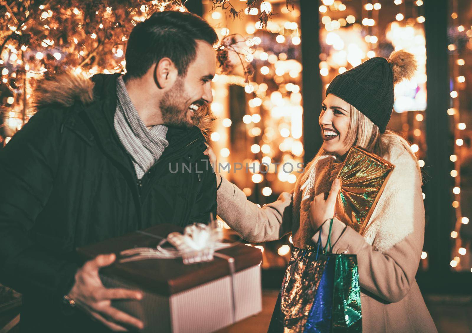 Young beautiful cheerful couple celebrating Christmas in the city street and giving many gift to each other. 