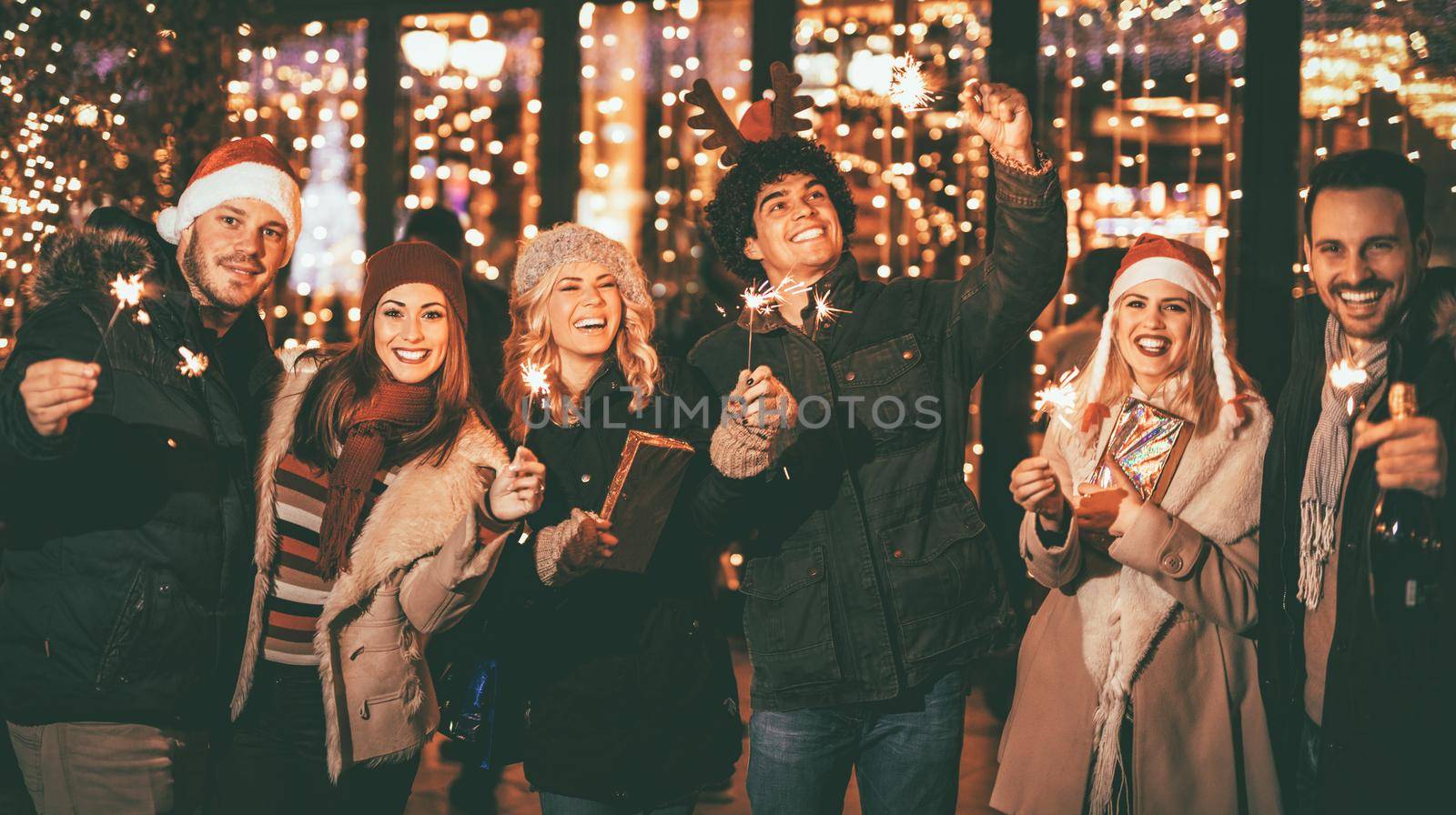 Three couple with sparklers enjoying Christmas outdoor party in the city street at night and with a lot of lights on background.