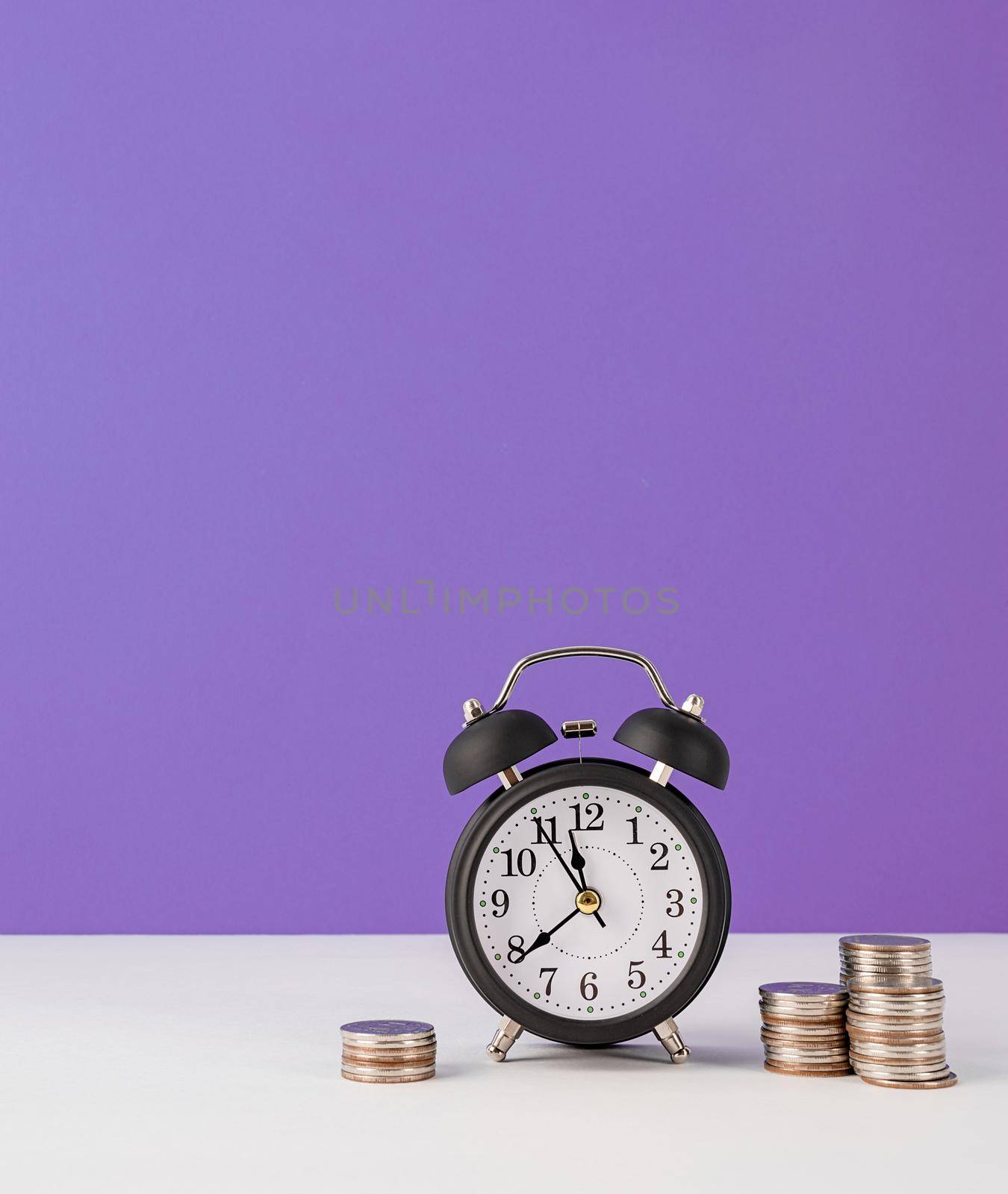 Time management, punctuality, business metaphors. Black vintage alarm clock with coins on purple background with copy space