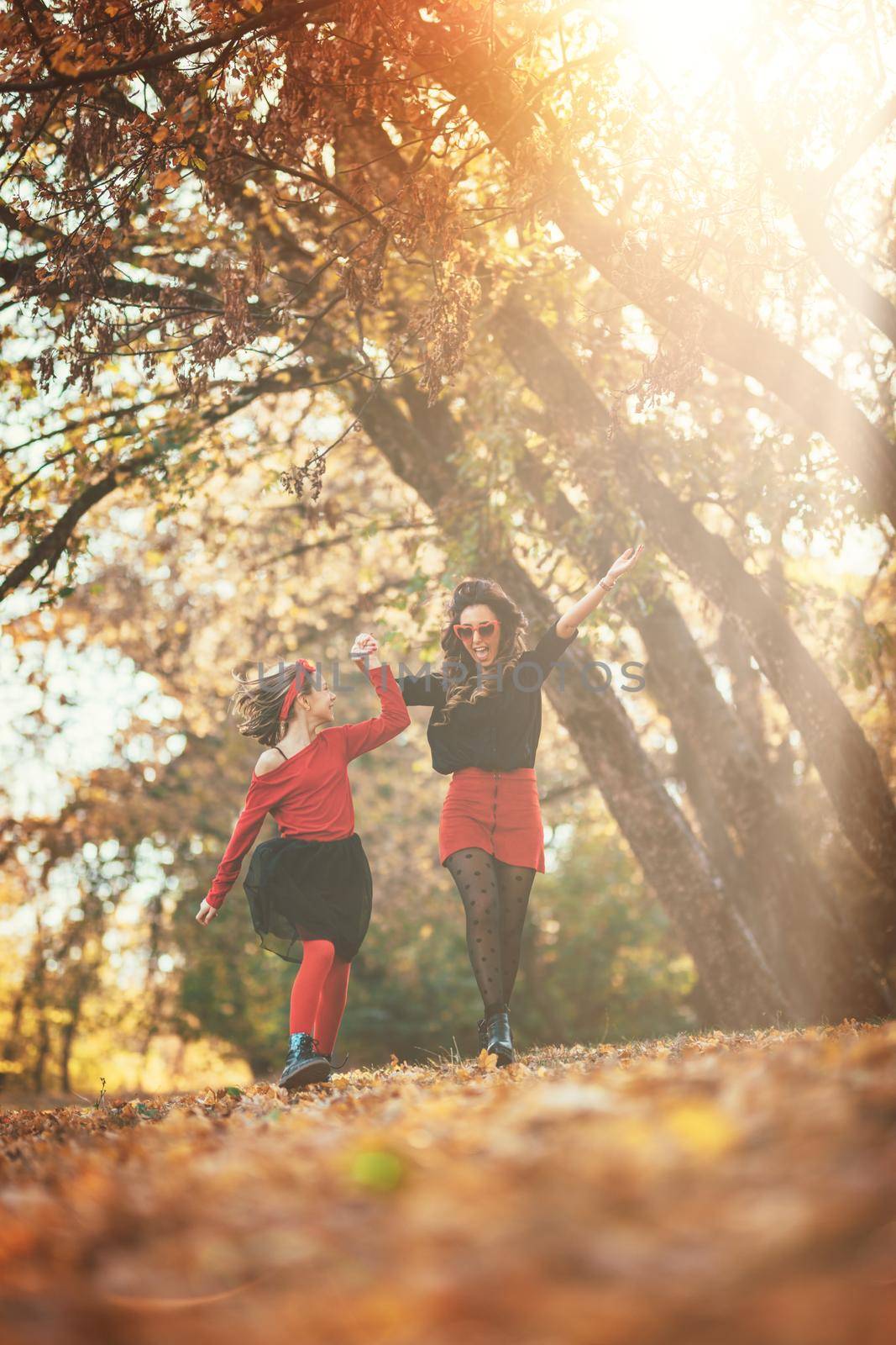 Beautiful young mother and her happy daughter having fun in the forest in sunset. They are holding hands, laughing and jumping.