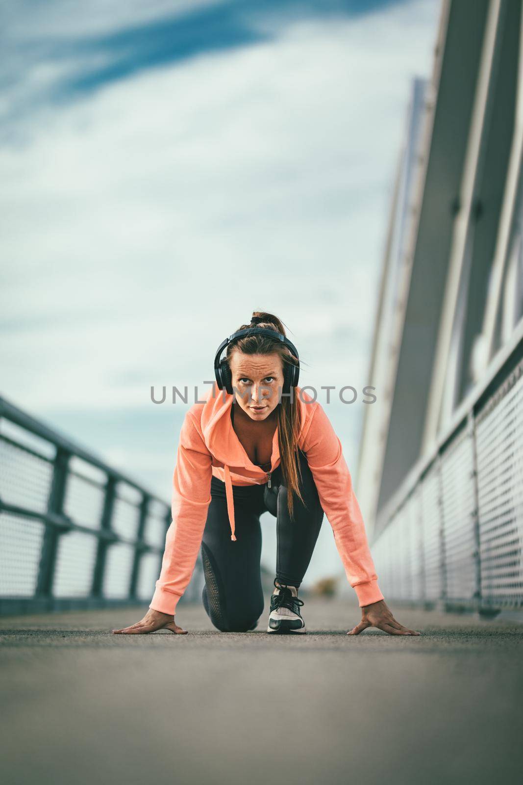 A young sport woman with headphones prepares for morning jogging on a river bridge.
