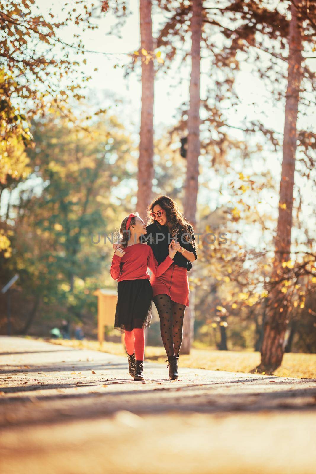 Beautiful young mother and her happy daughter having fun in the forest in sunset. They are holding hands, laughing and walking.