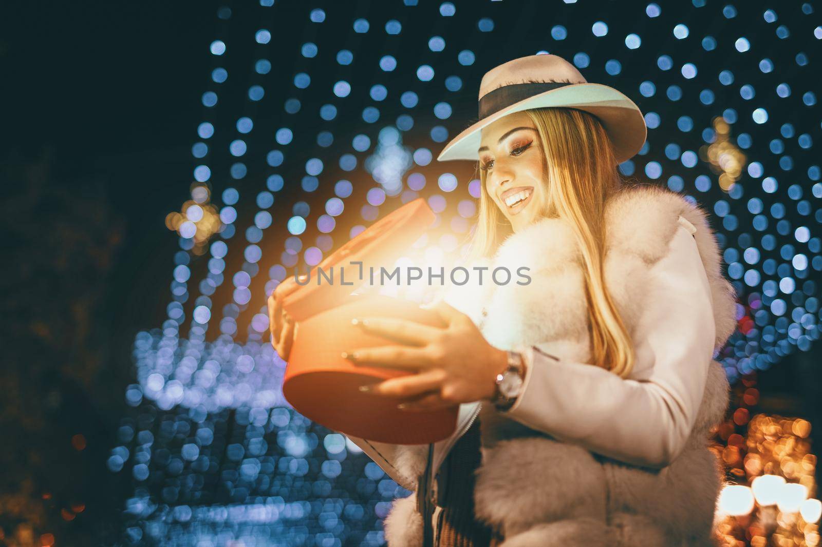 Cheerful young woman with red present having fun in the city street at Christmas time.