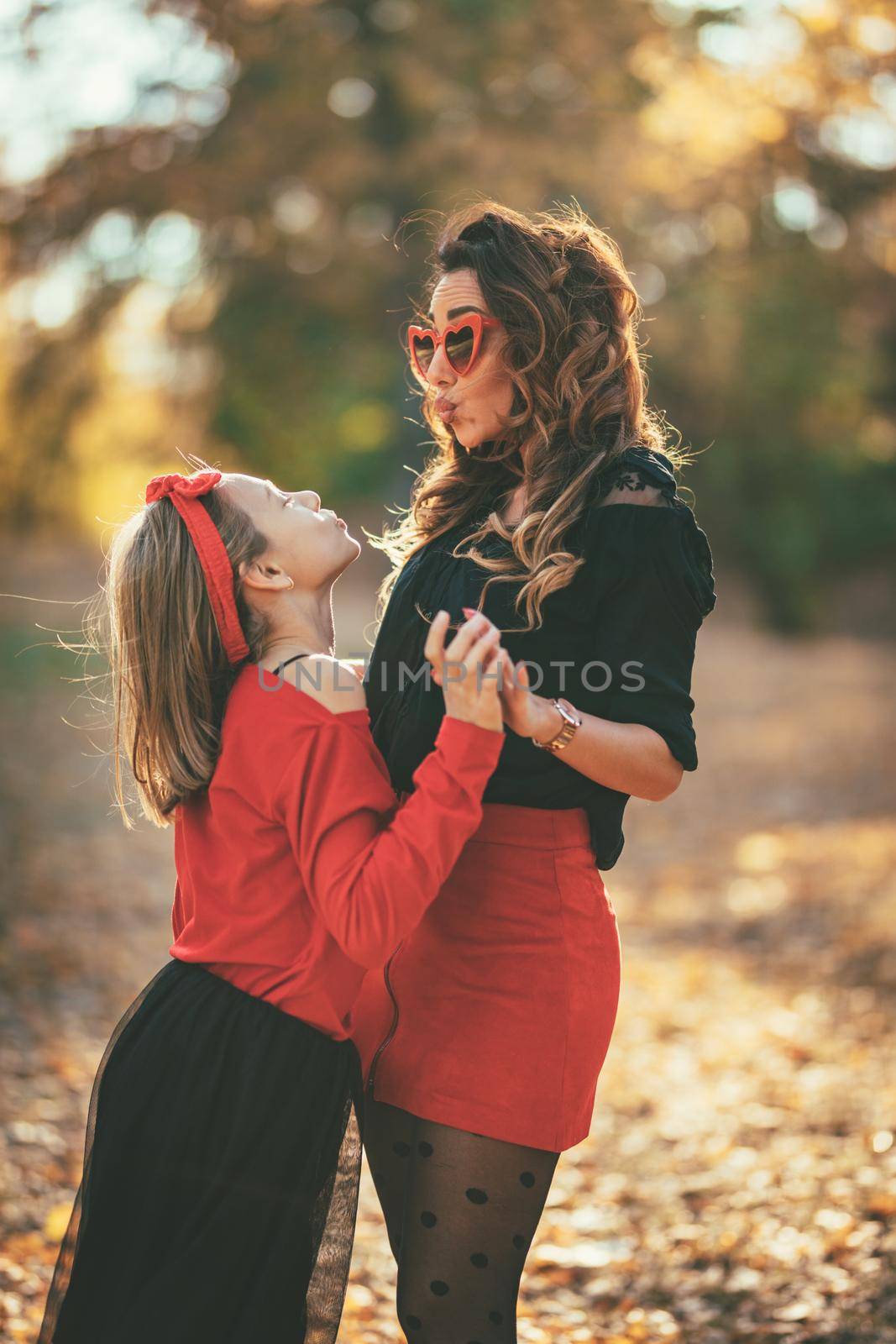 Beautiful young mother and her happy daughter having fun in the forest in sunset. They are hugging, smiling and looking each other.