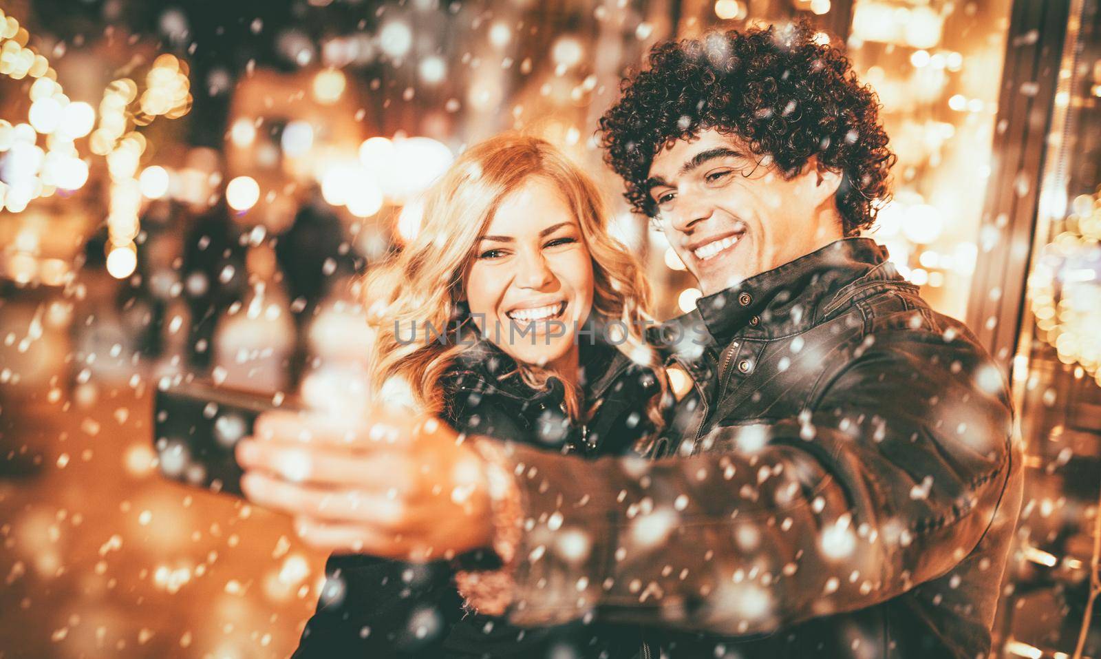 Two beautiful cheerful young people taking selfie in the street with snowflakes surrounding. 