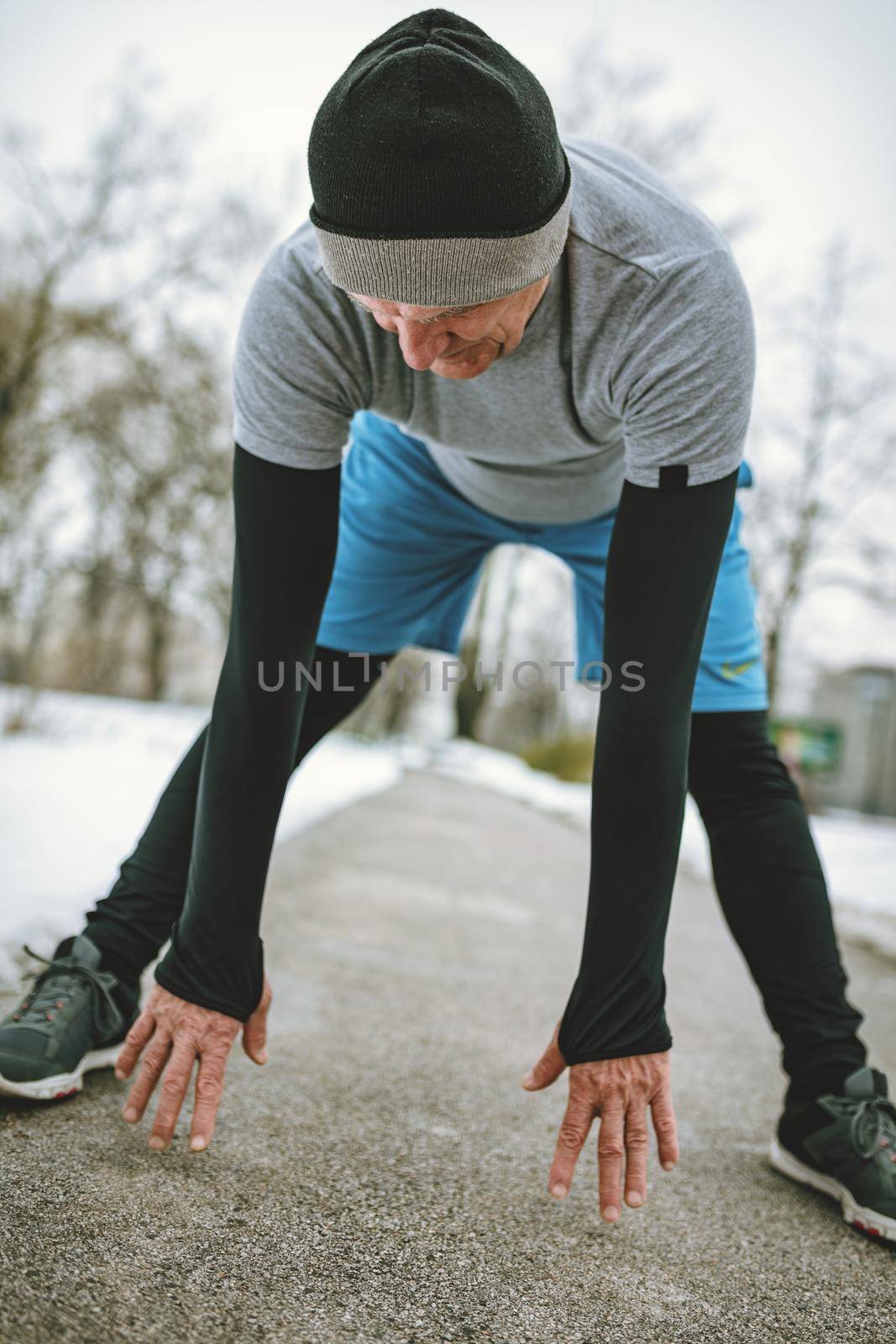 Active senior man stretching and doing exercises in public park during the winter training outside in.