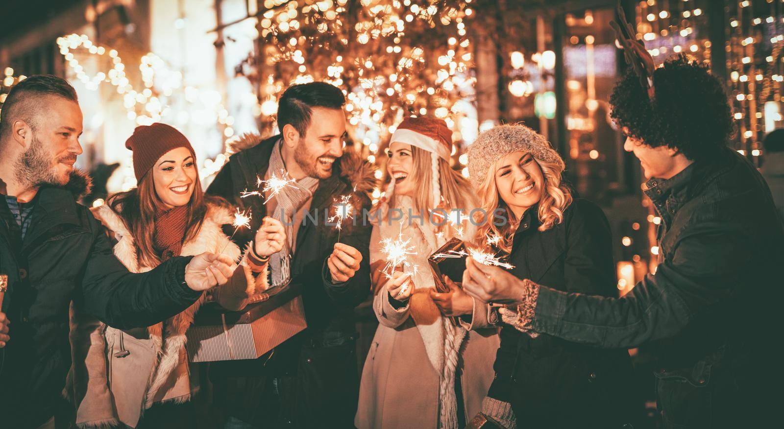 Three couple with sparklers enjoying Christmas outdoor party in the city street at night and with a lot of lights on background.