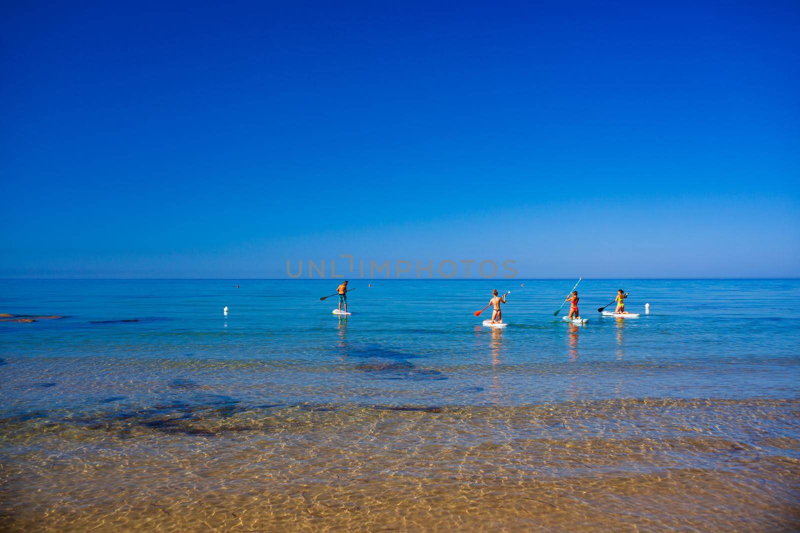 Stand up paddle boarding. Joyful group of friendsare training SUP board in the mediterranean sea on a sunny morning in Realmonte beach, Sicily. Italy