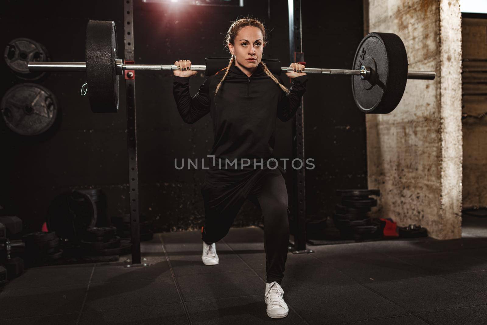 Young muscular beautiful woman doing lunges exercise with barbell at the gym. 