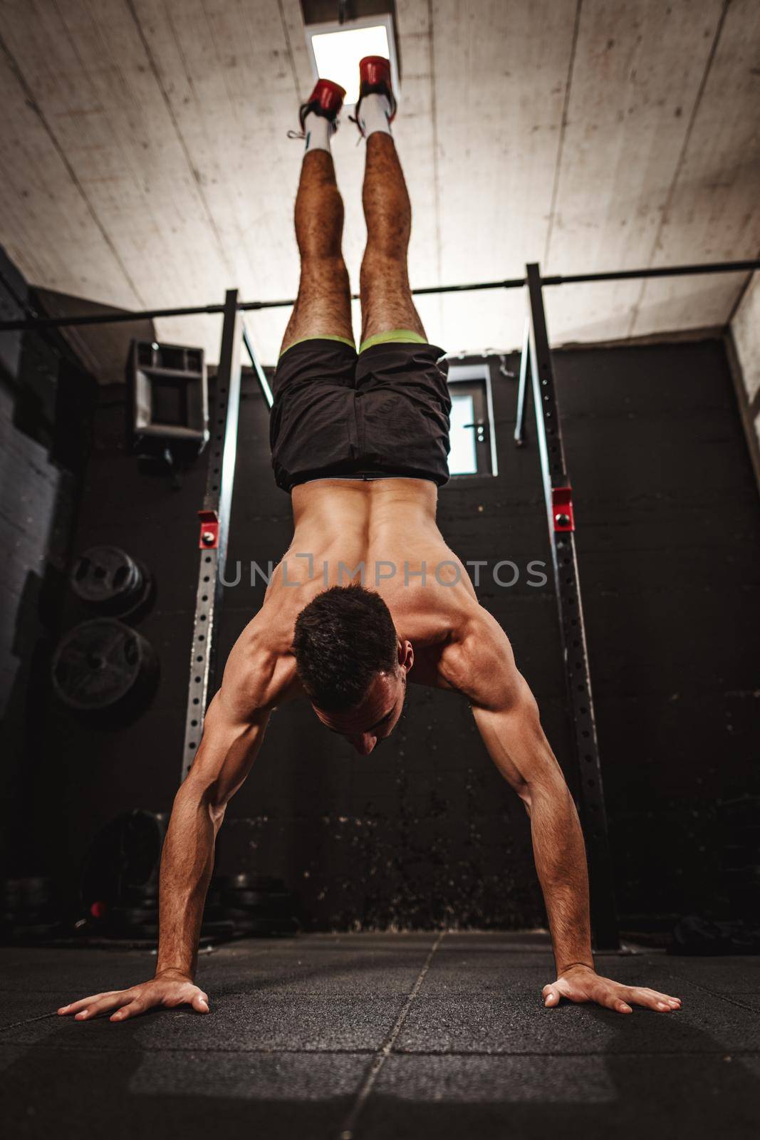 Young muscular man doing hard exercise at the gym. His is doing handstand and whole weight is on his hands.