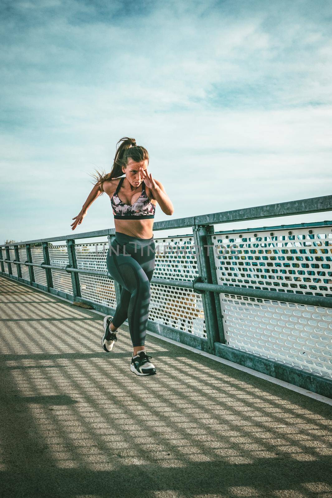 Fit muscular young woman runner sprinting at great speed outdoors on the river bridge.