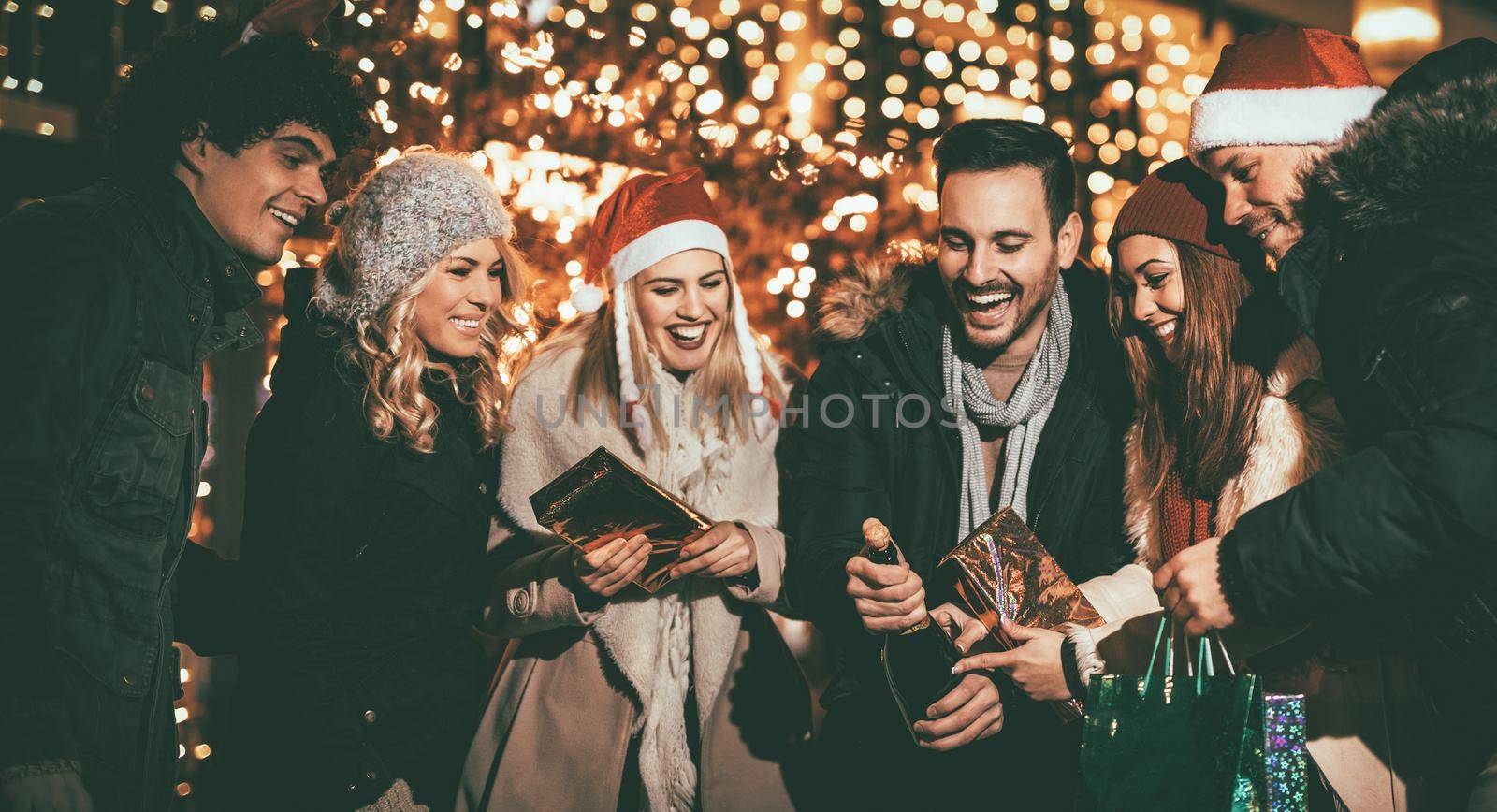 Three young couple having fun at the Christmas outdoor party in the city street at night and with a lot of lights on background.