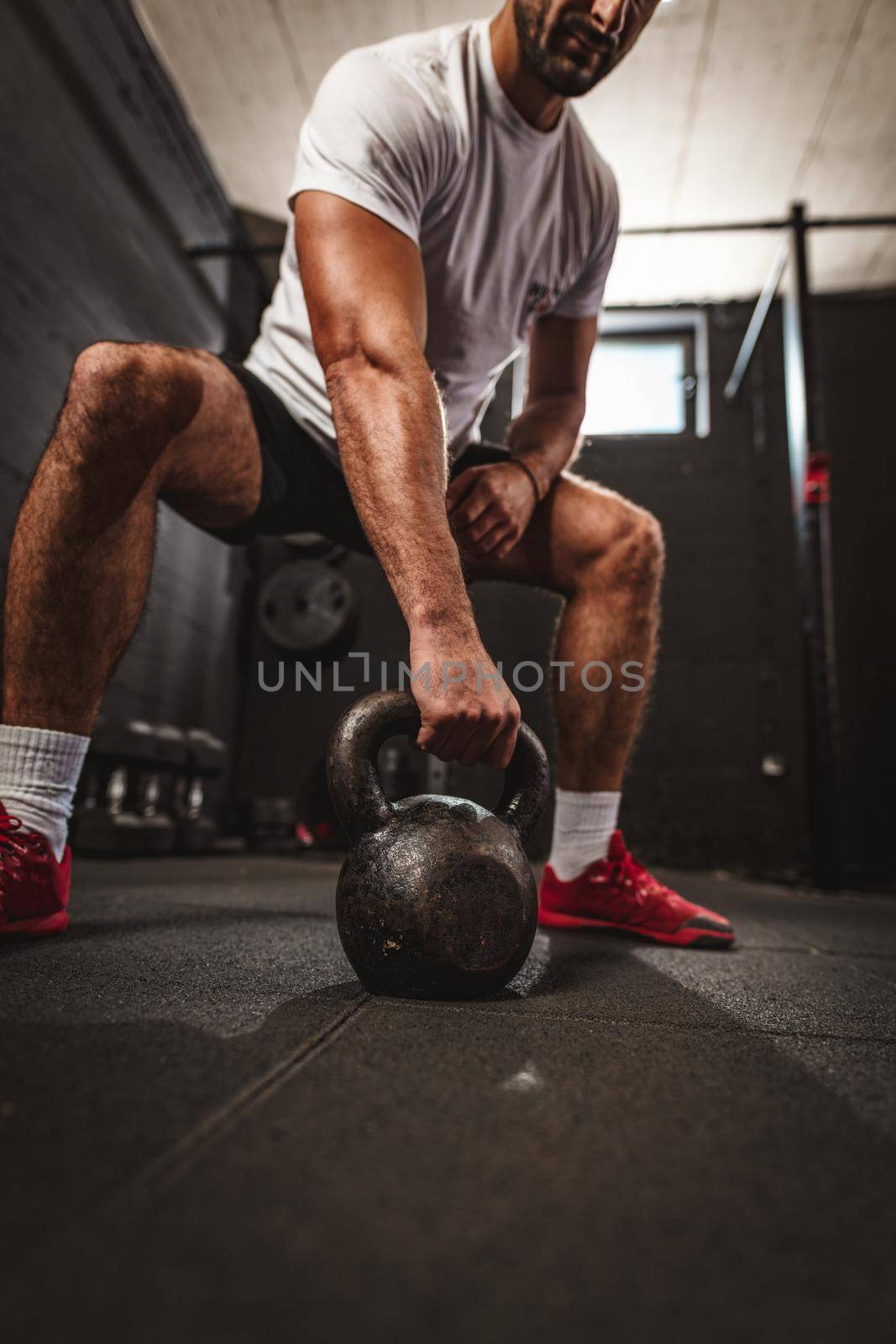 Young muscular man doing hard exercise with kettlebell on cross training at the gym.