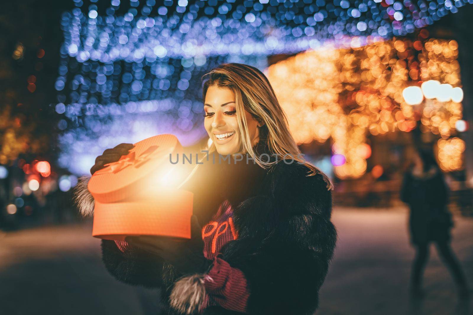 Cheerful young woman with red present having fun in the city street at Christmas time.