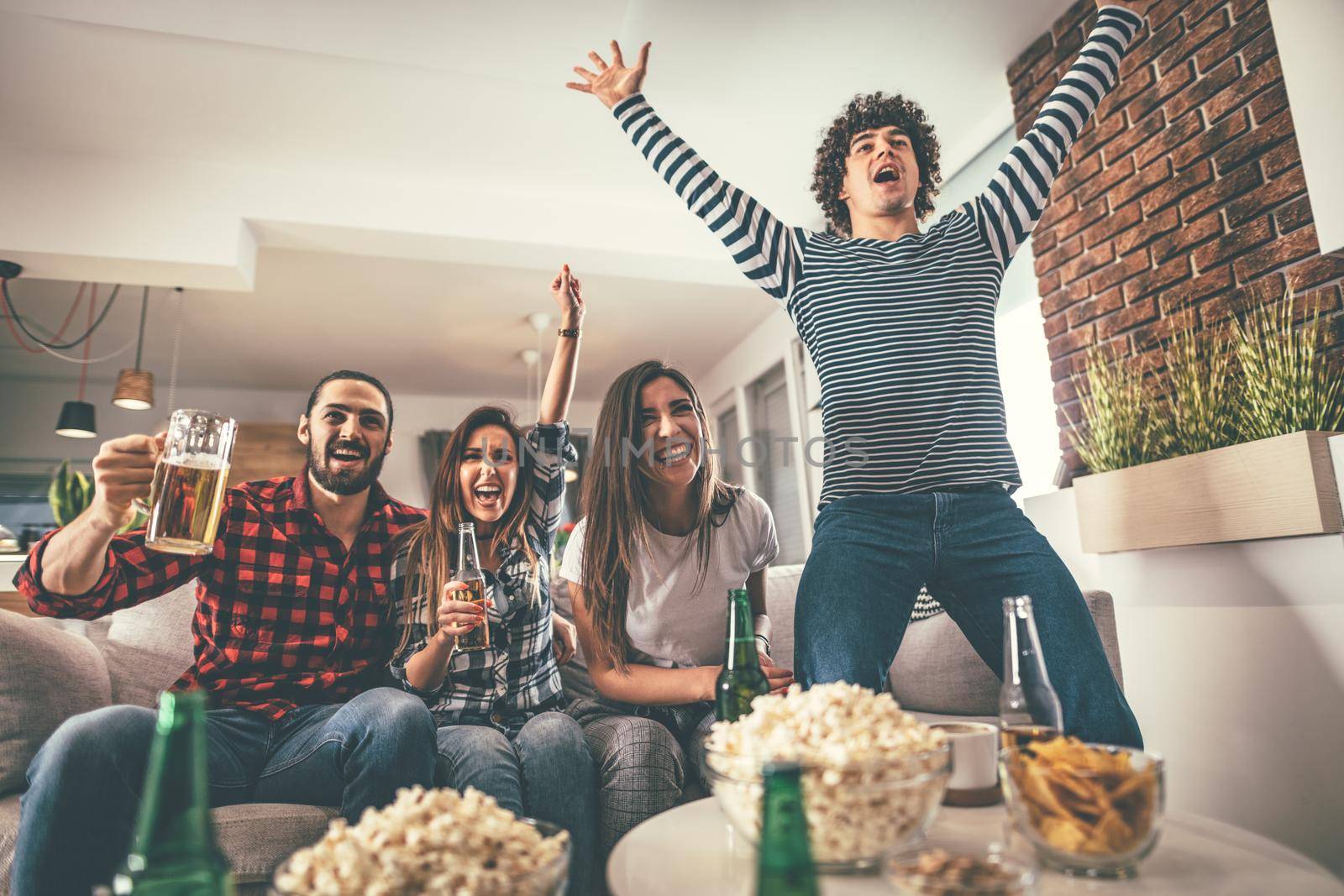 Friends are fans of sports games as football love spending their free time at home together. They are screaming and gesturing for a victory. 