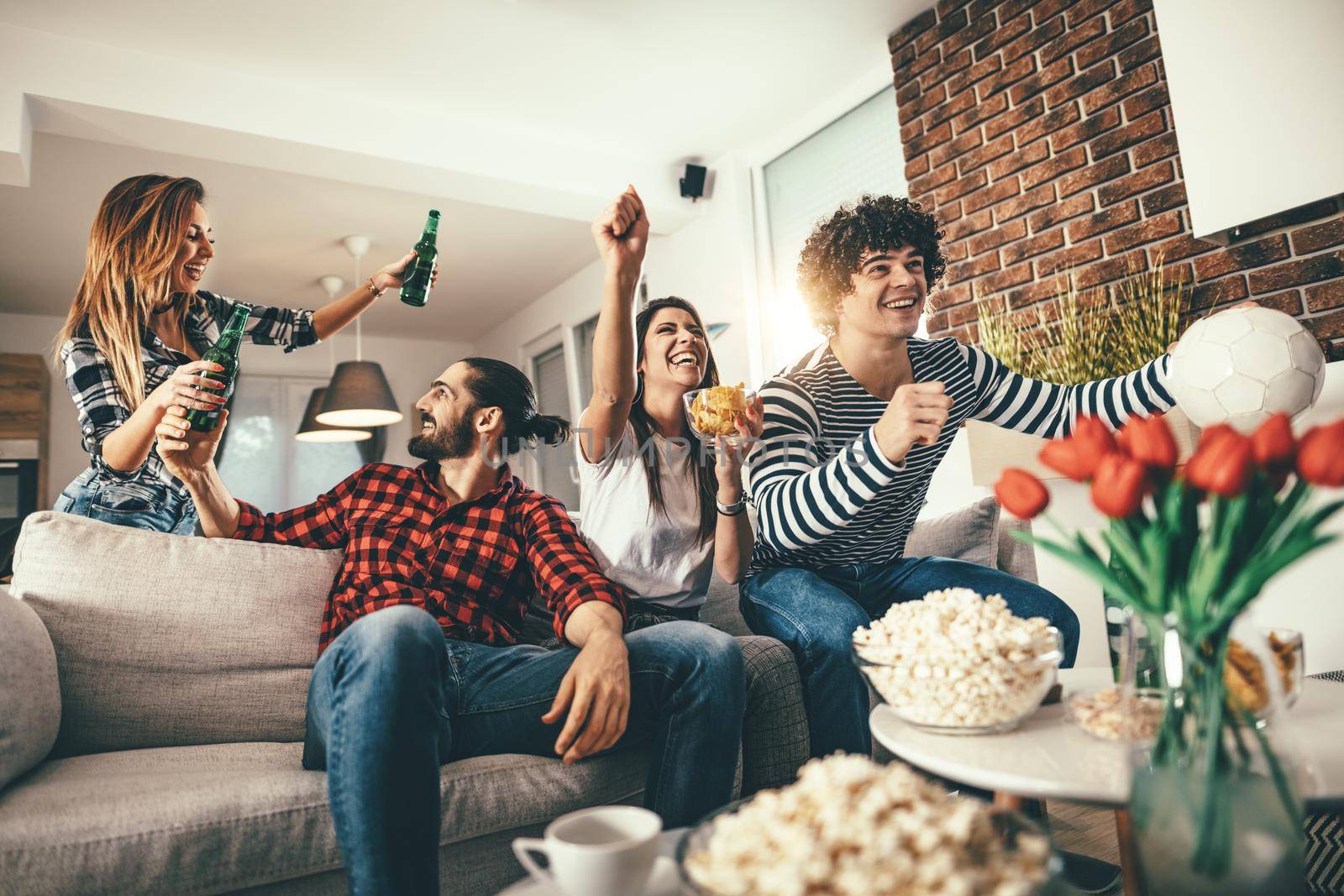 Friends are fans of sports games as football love spending their free time at home together. They are screaming and gesturing for a victory. 