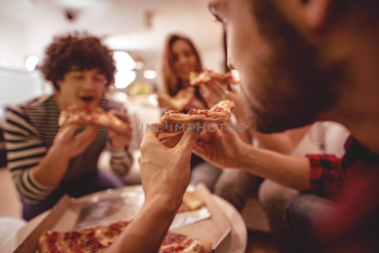 Happy friends having fun while eating pizza. They have great weekend in nice company indoors. 