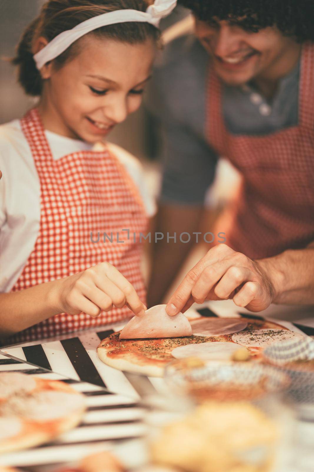 Little girl and her father are putting ketchup and origano on the pizza.