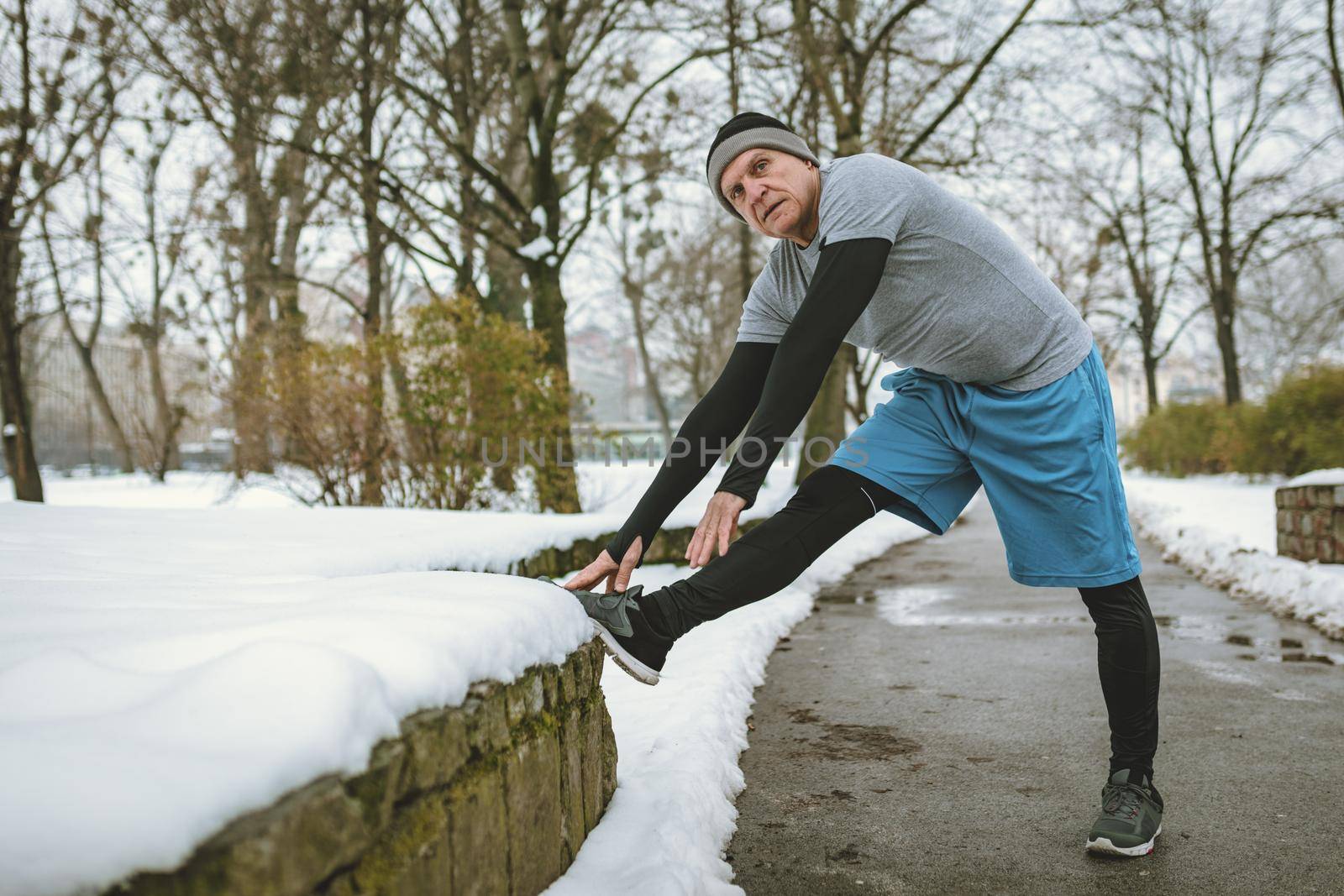 Active senior man stretching and doing exercises in public park during the winter training outside in.