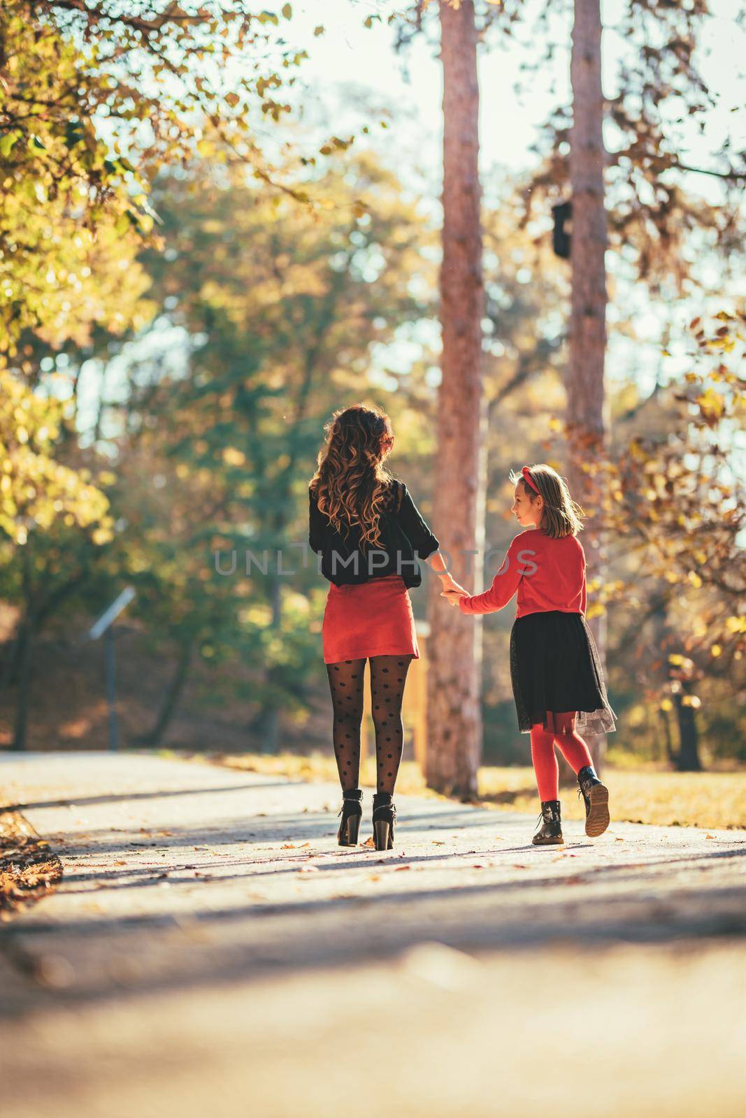 Beautiful young mother and her happy daughter having fun in the forest in sunset. They are holding hands, laughing and walking.