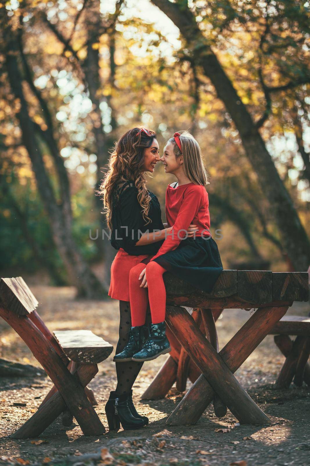 Beautiful young mother and her happy daughter having fun in the forest in sunset. They are hugging, smiling and looking each other.